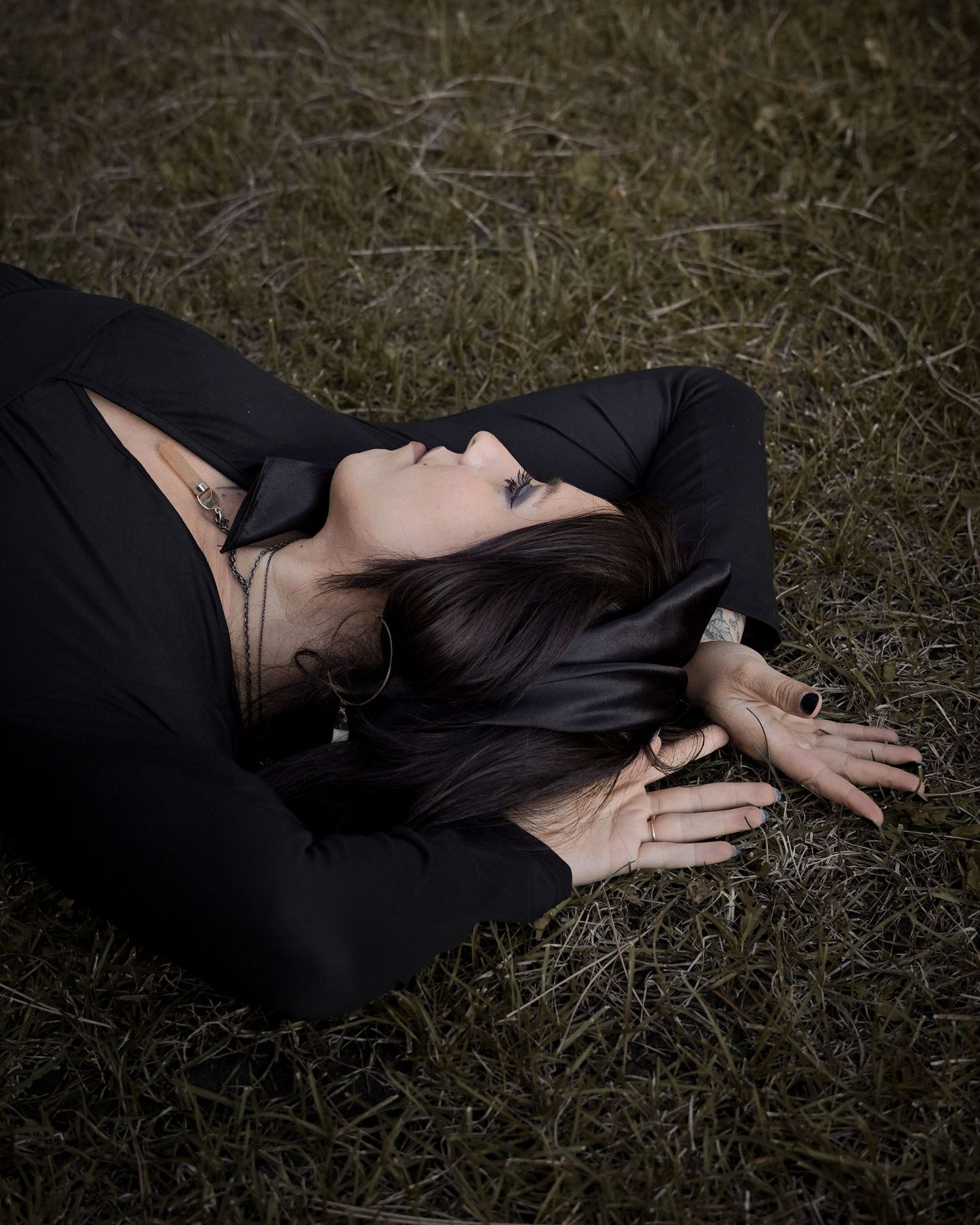 Person wearing black clothing lies on grass in artistic moody outdoor portrait.