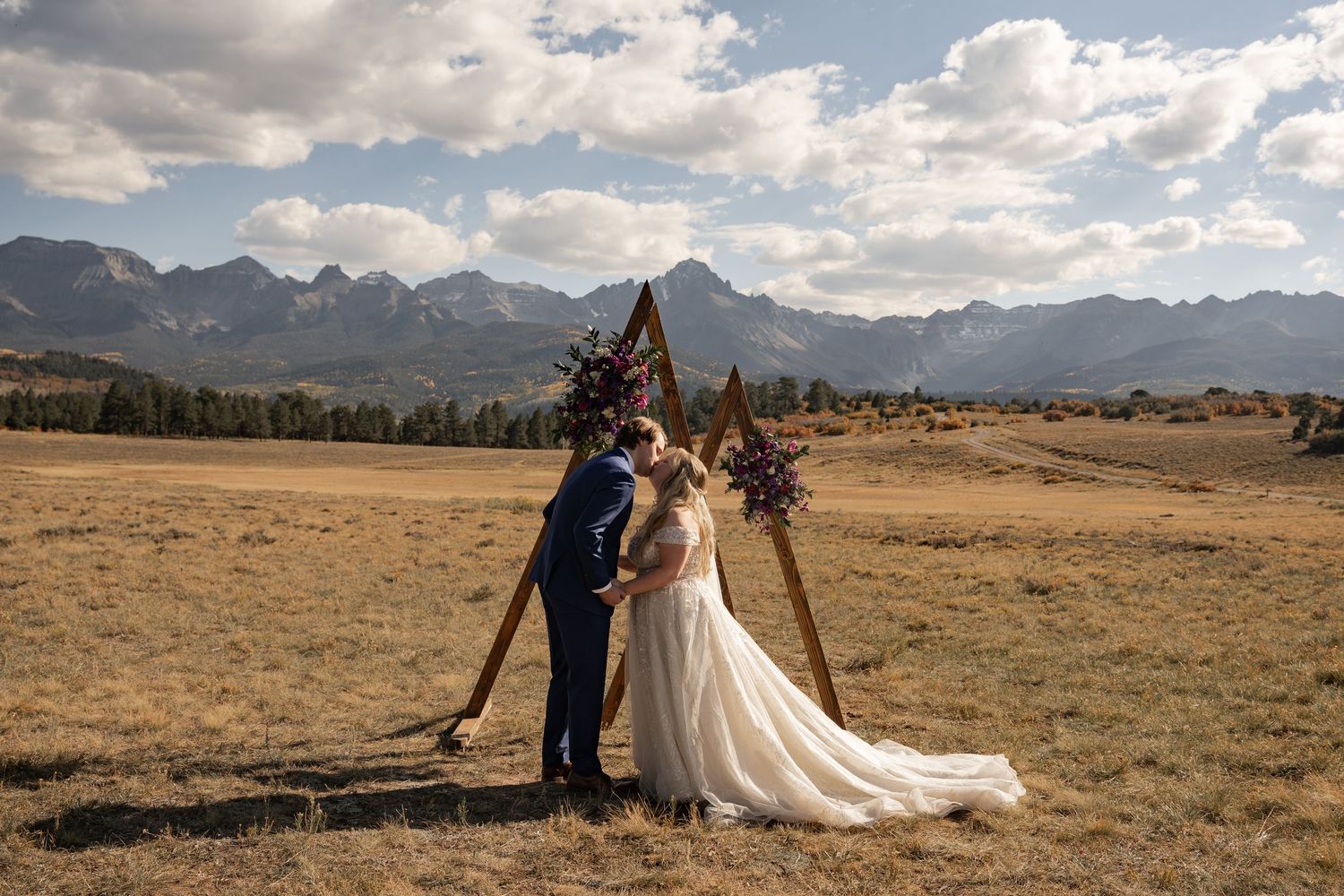 Wedding couple photographed in an expansive mountain field with dramatic cloudy skies.