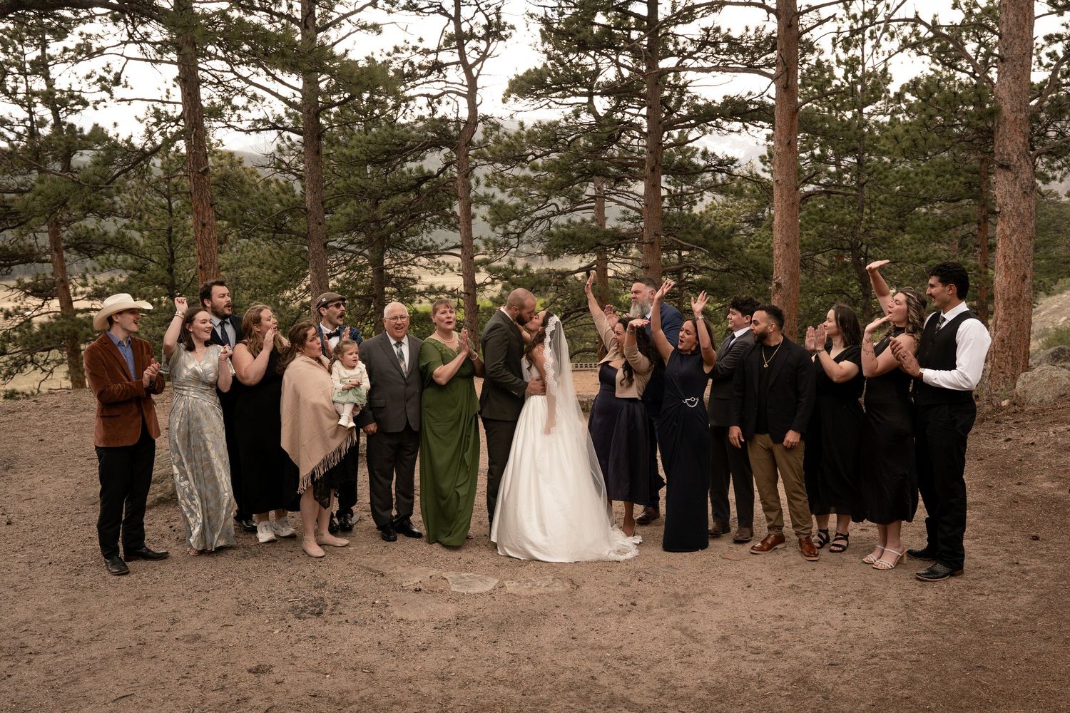 Wedding party celebrates with cheers among pine trees at a rustic outdoor Colorado mountain wedding.