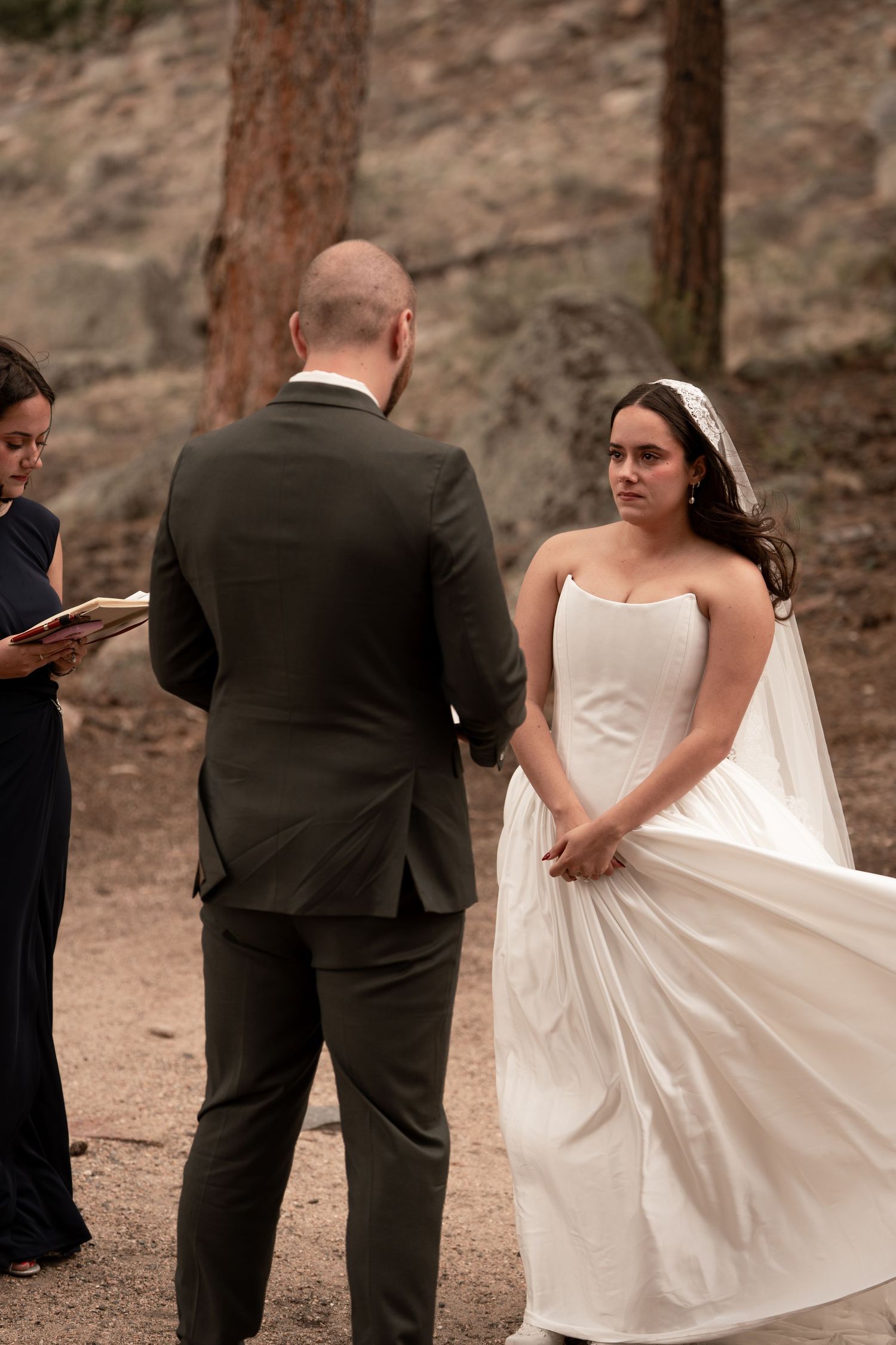 Bride in white gown and veil exchanges vows with groom in dark suit during outdoor wedding ceremony.