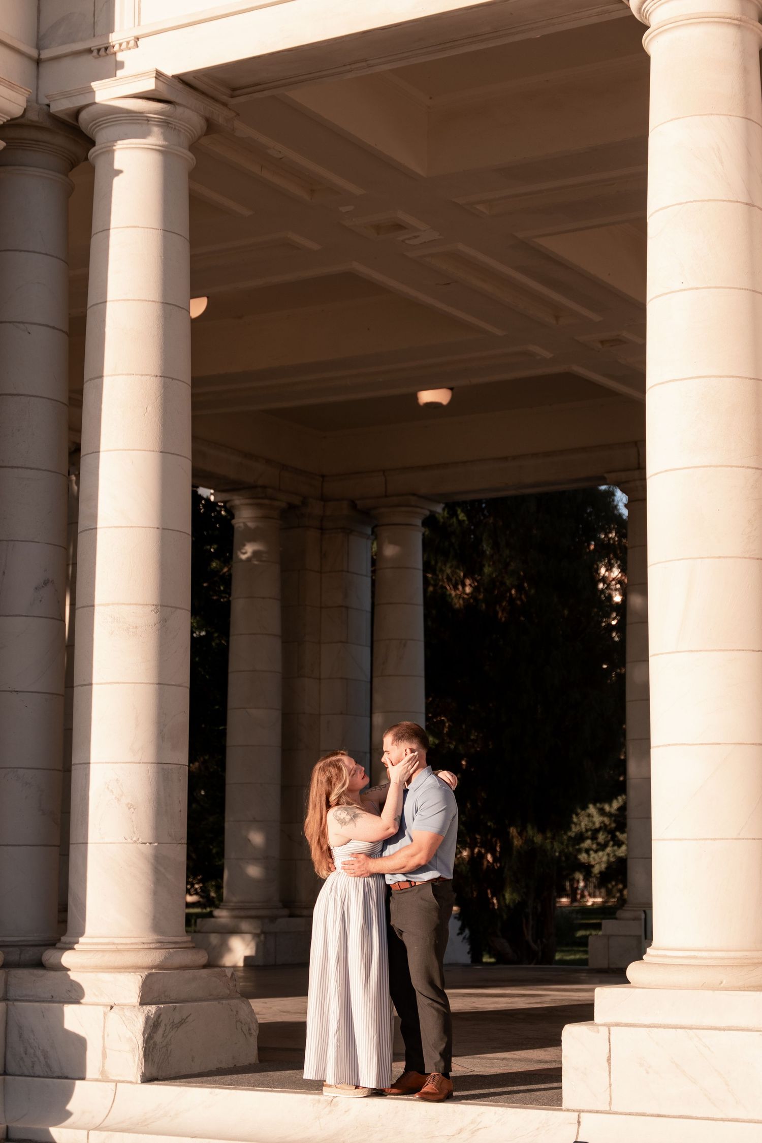 Couple embracing romantically between elegant stone columns of a classical building at golden hour.