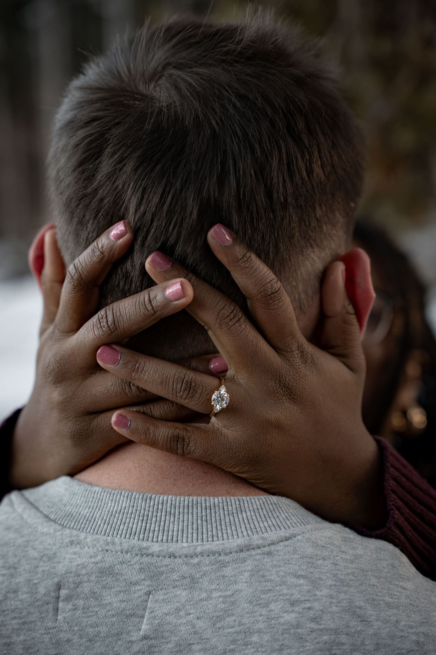 Close-up of woman's hands with pink nails and diamond engagement ring embracing man's head.