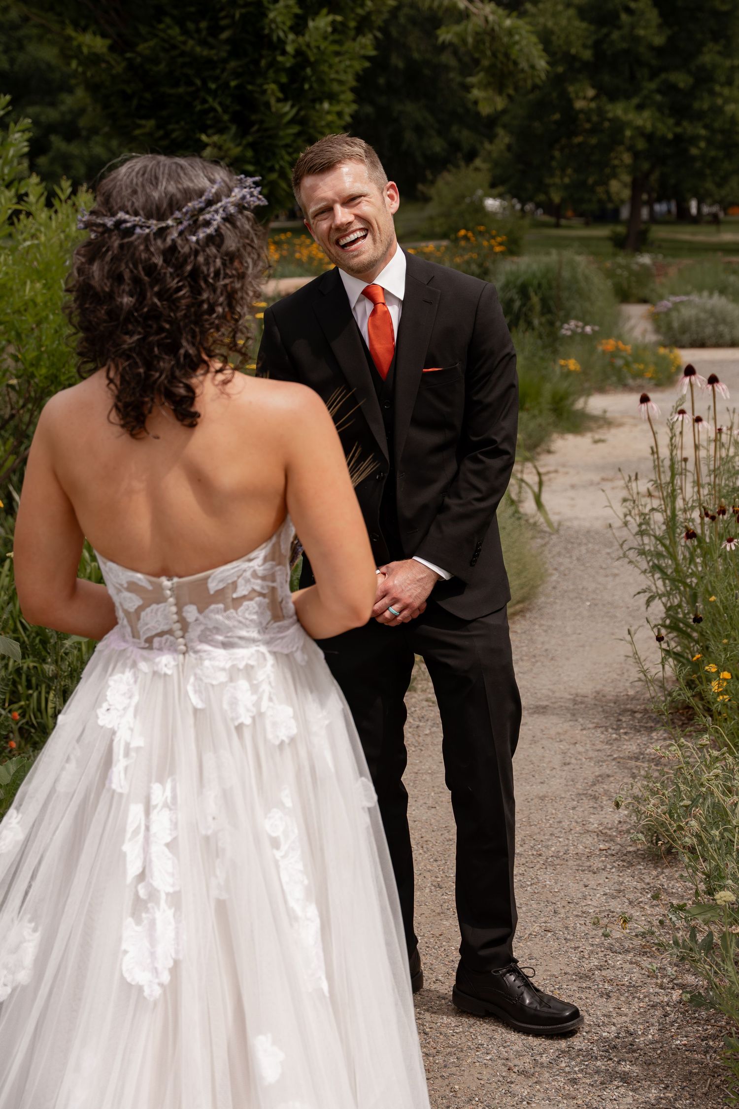 A couple in wedding attire shares a candid moment together on a garden path surrounded by wildflowers.