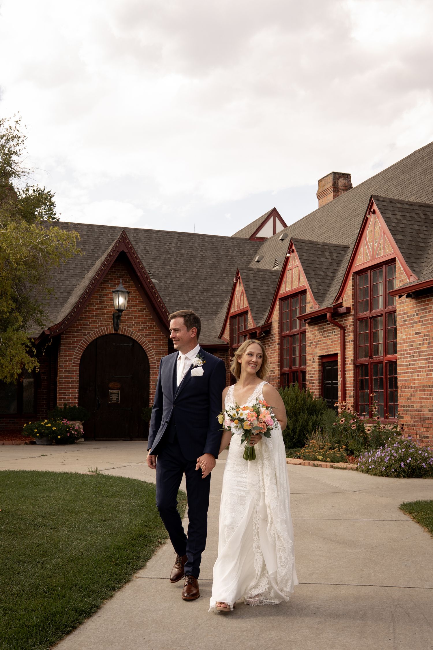 Couple walks together outside brick wedding venue with arched entrance.