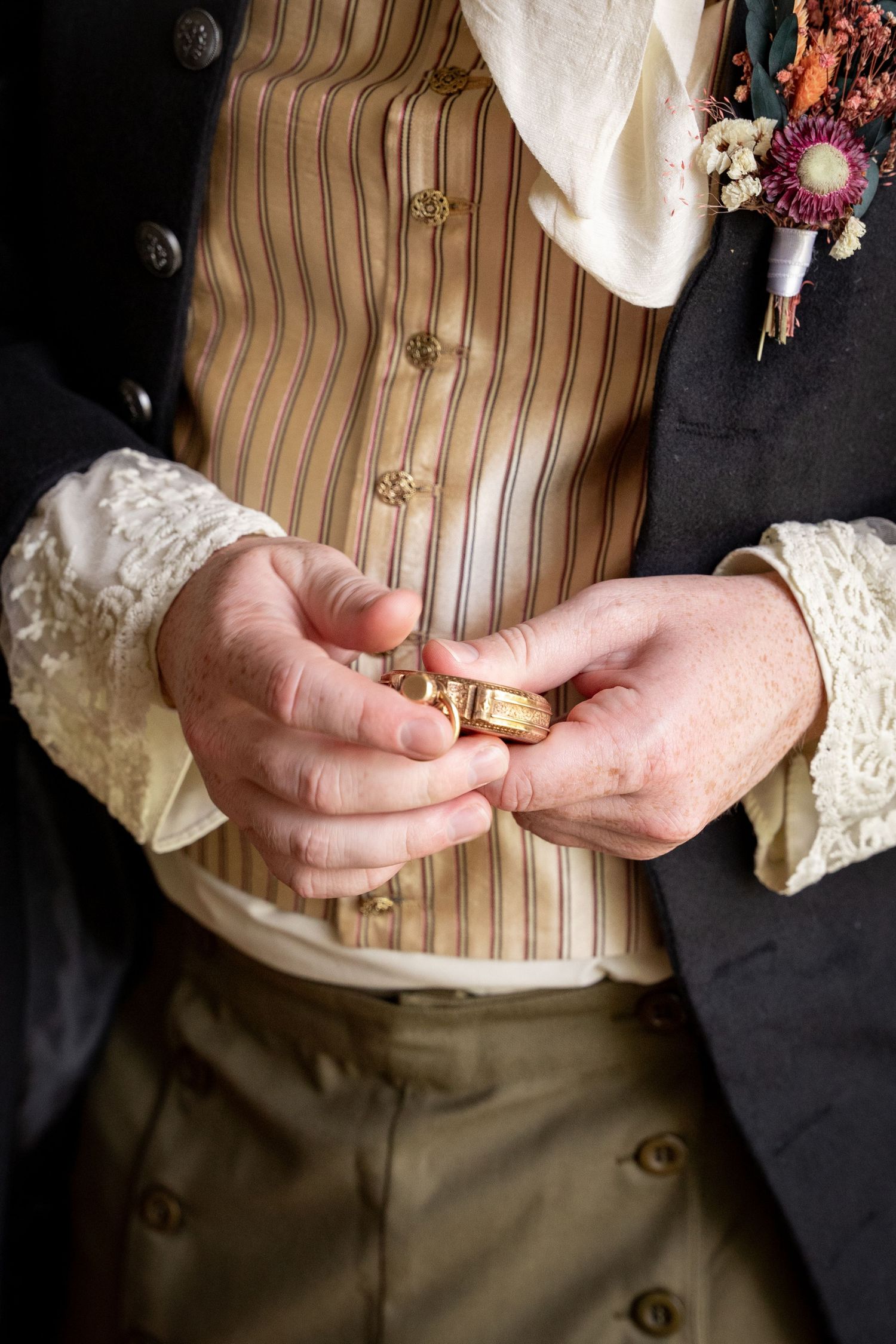 Groom to be holds a vintage pocket watch in his hands as he's getting ready.