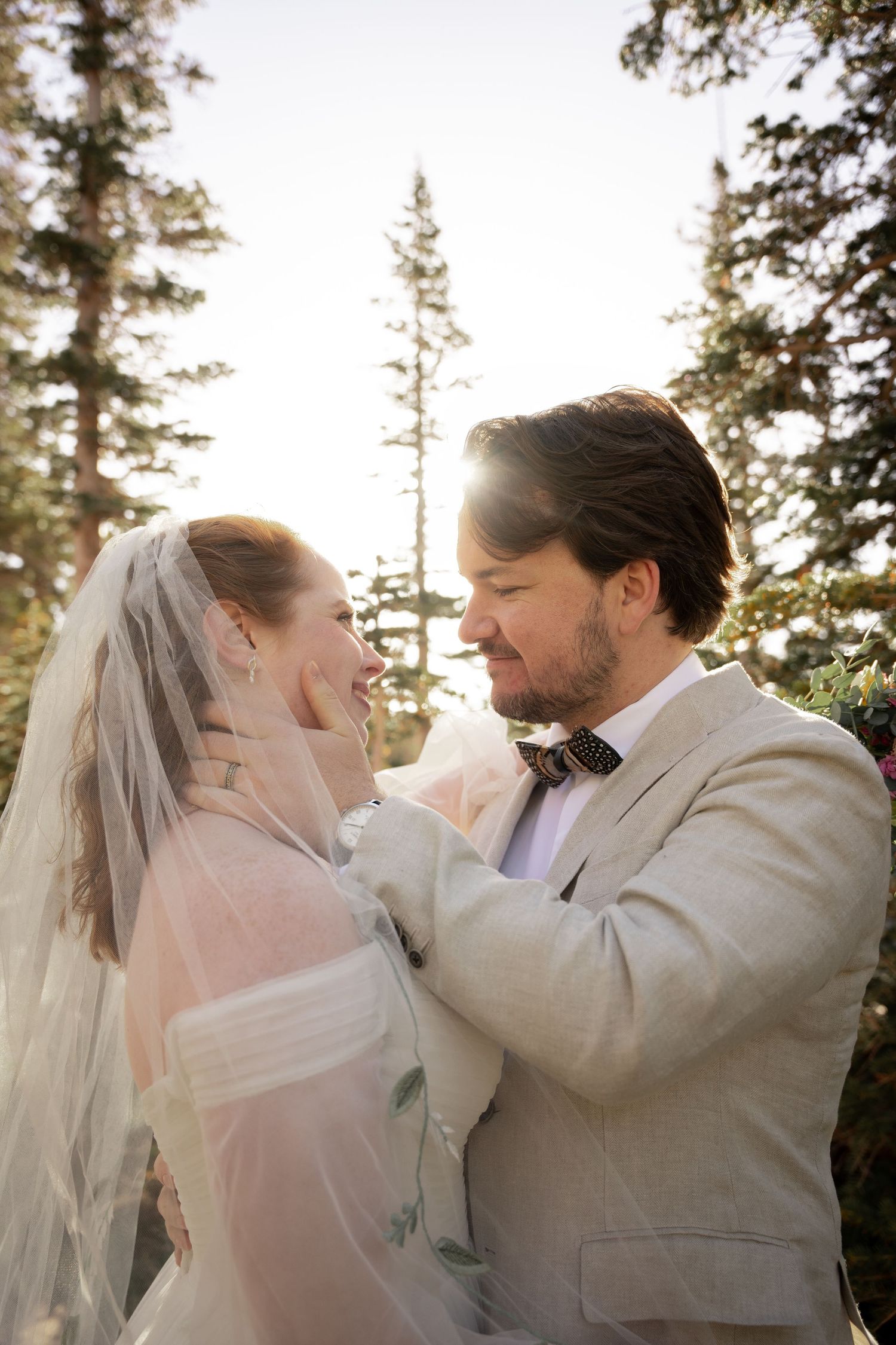 Romantic first kiss moment between newlyweds surrounded by towering evergreen trees.