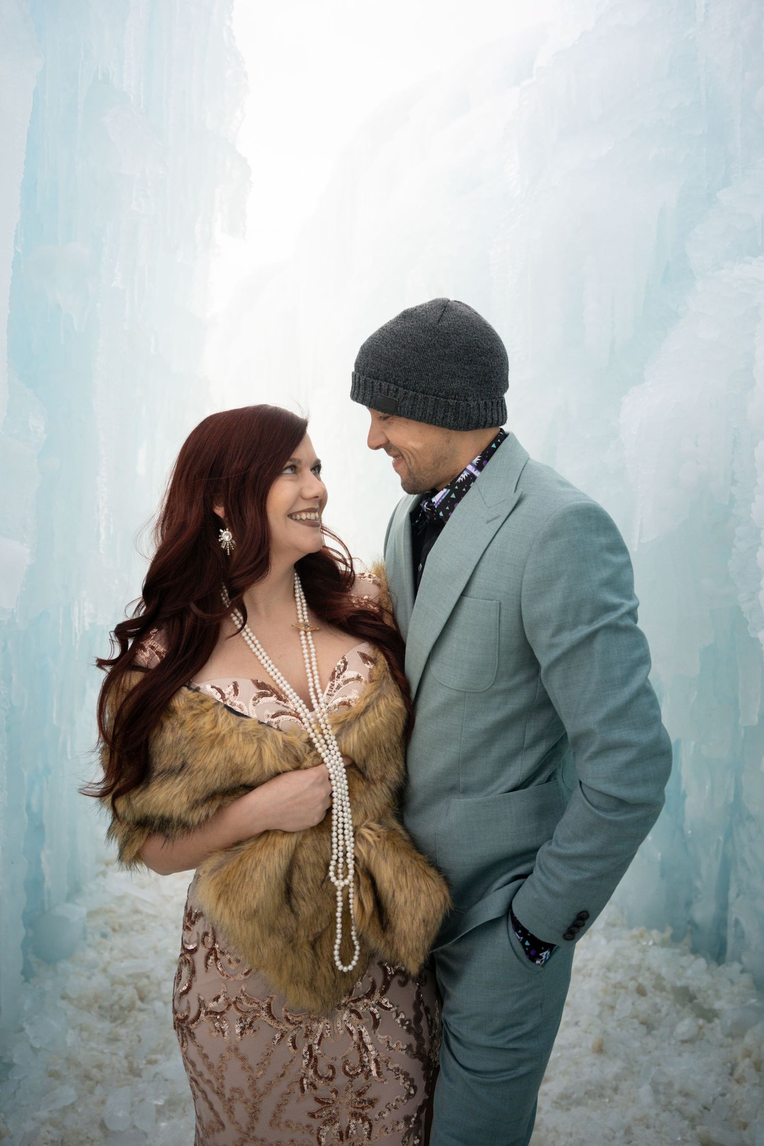 Winter engagement photos against icy blue backdrop with couple in formal attire.