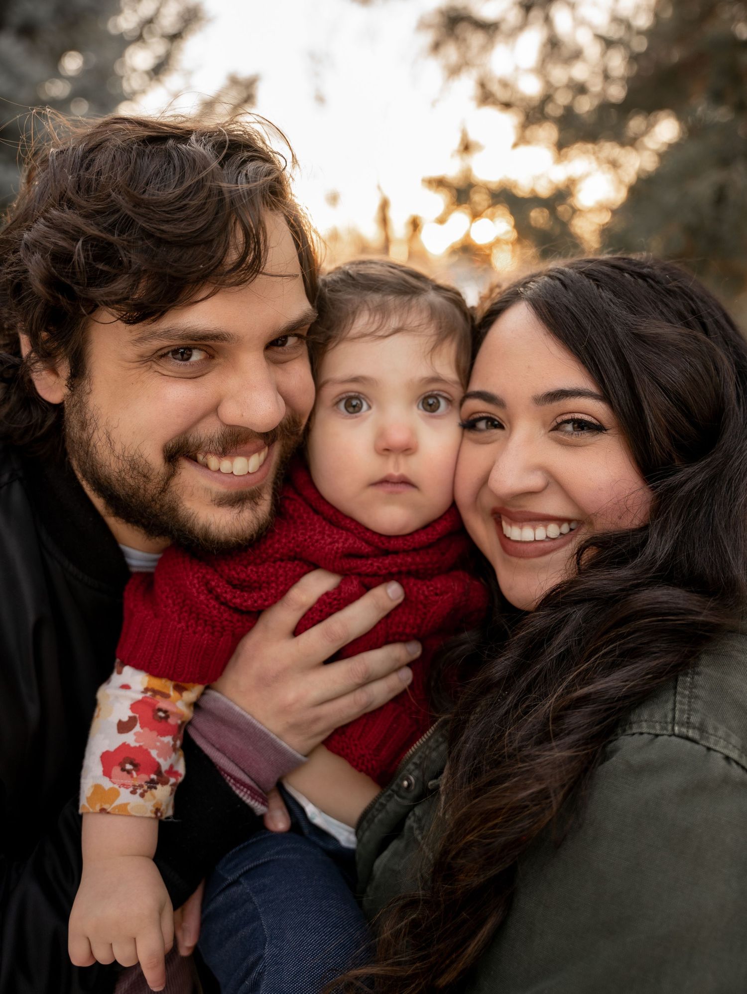 Happy young family with smiling parents holding their baby outdoors in warm golden hour light.