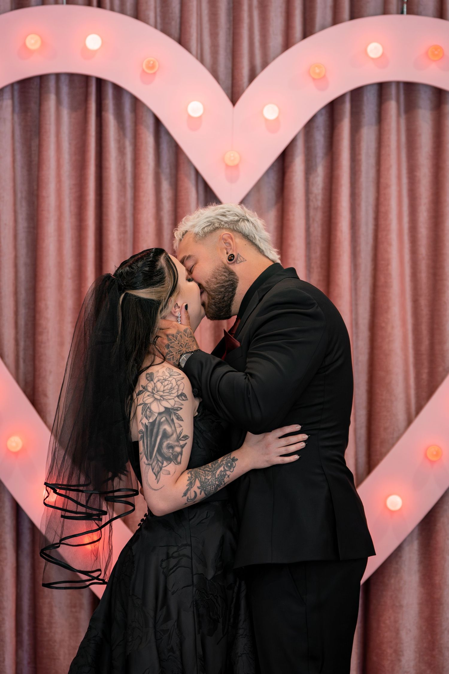Romantic couple embracing against pink curtain backdrop with illuminated heart decorations.