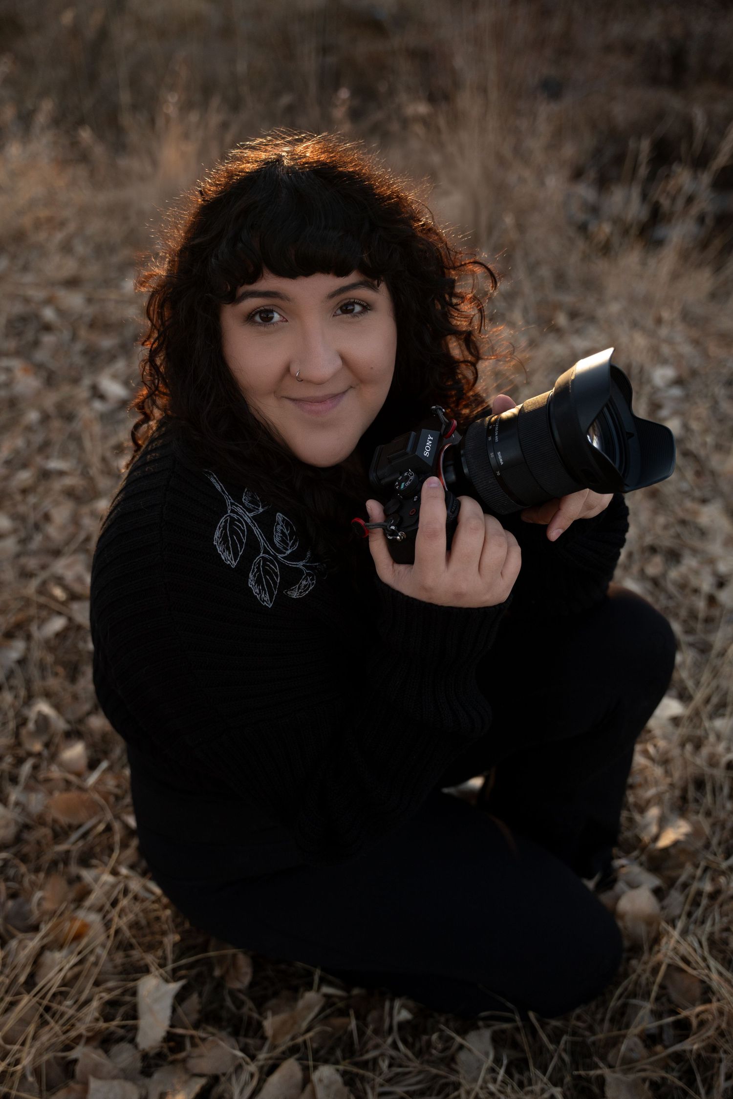 Photographer in black clothing lying in autumn field with camera.