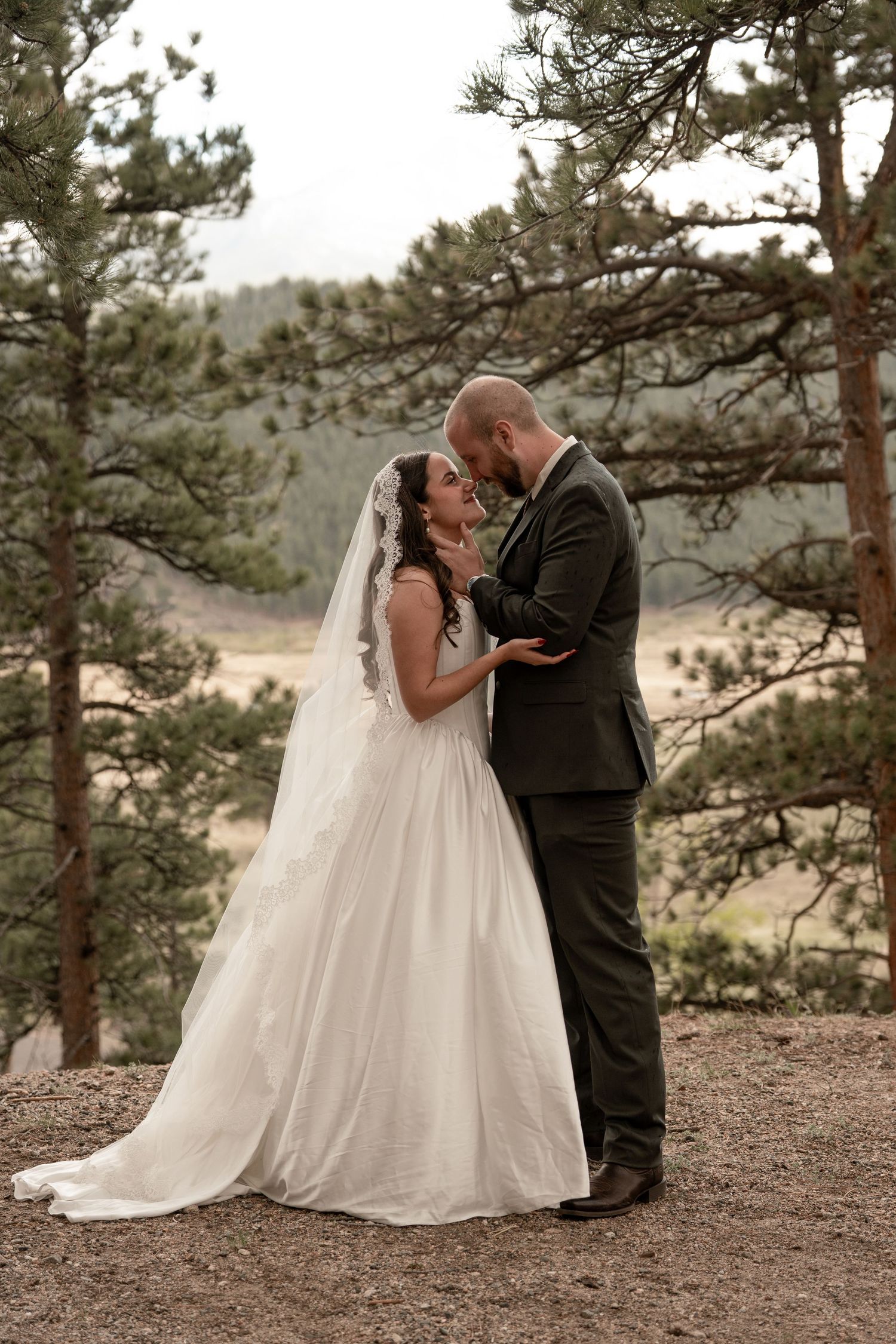 Bride and groom share a romantic moment among pine trees with mountain valley views on their wedding day.