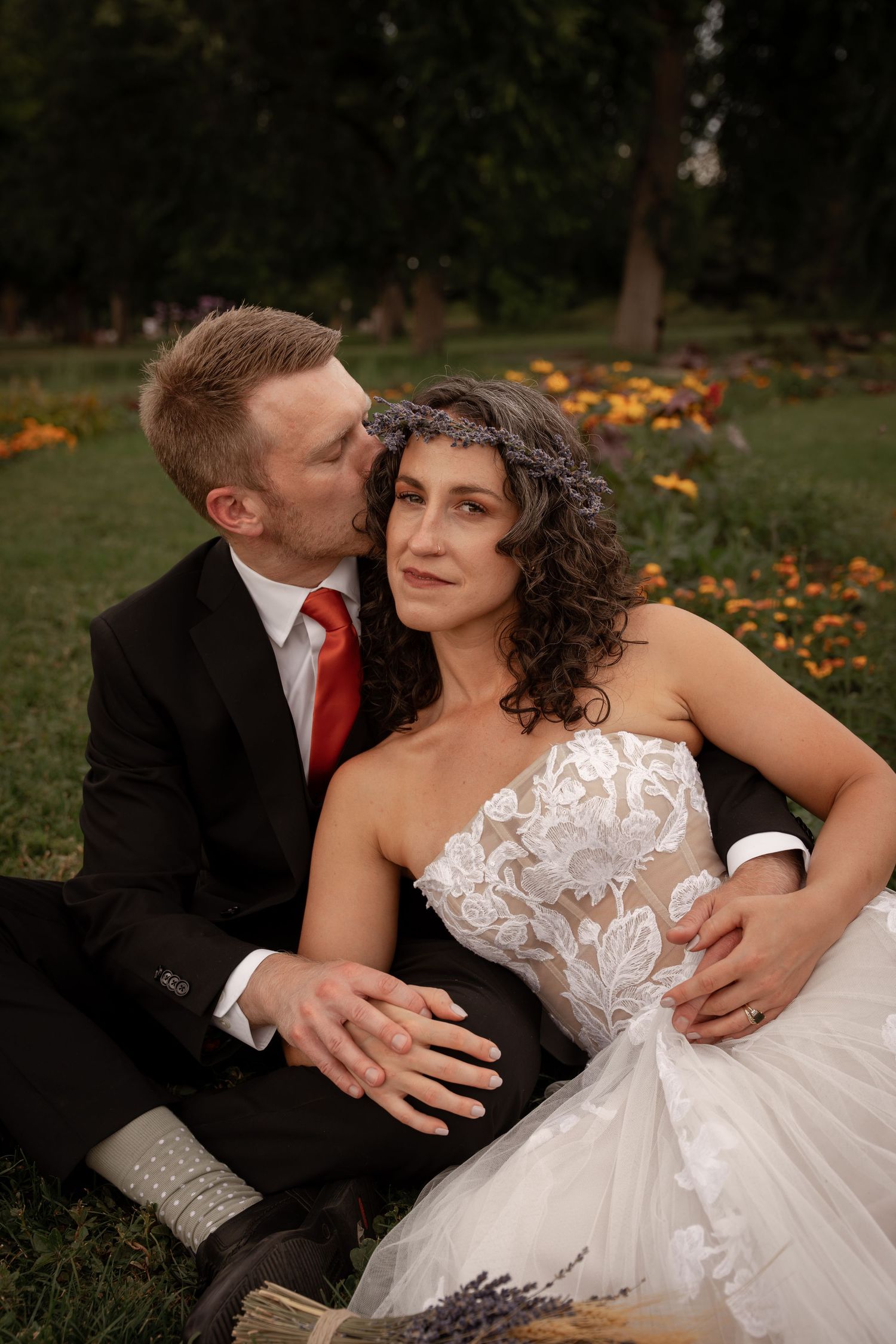 A romantic wedding couple embracing on grass with orange flowers in the background.