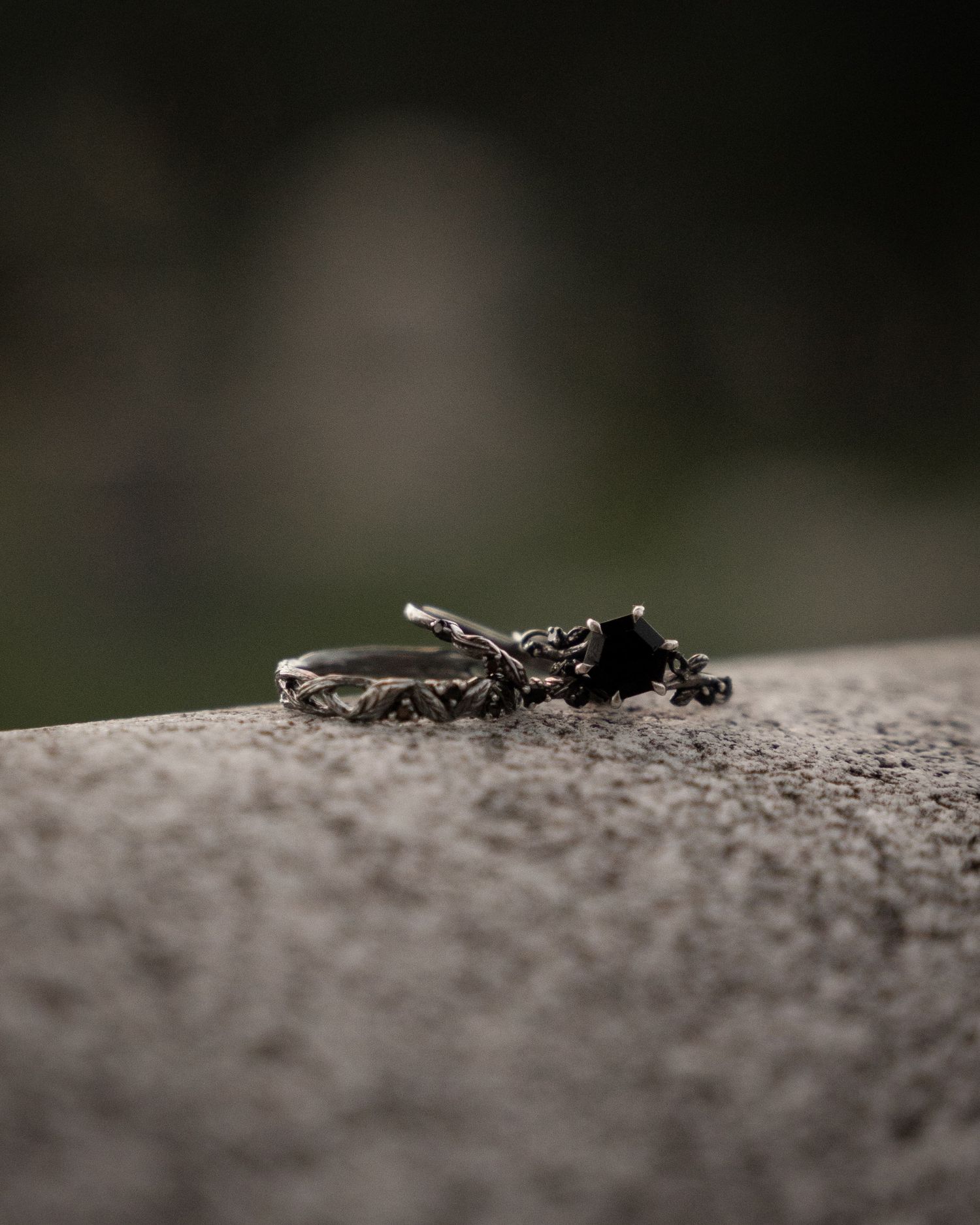 Gothic silver ring with black gemstone and twig design resting on stone surface with dark bokeh background.