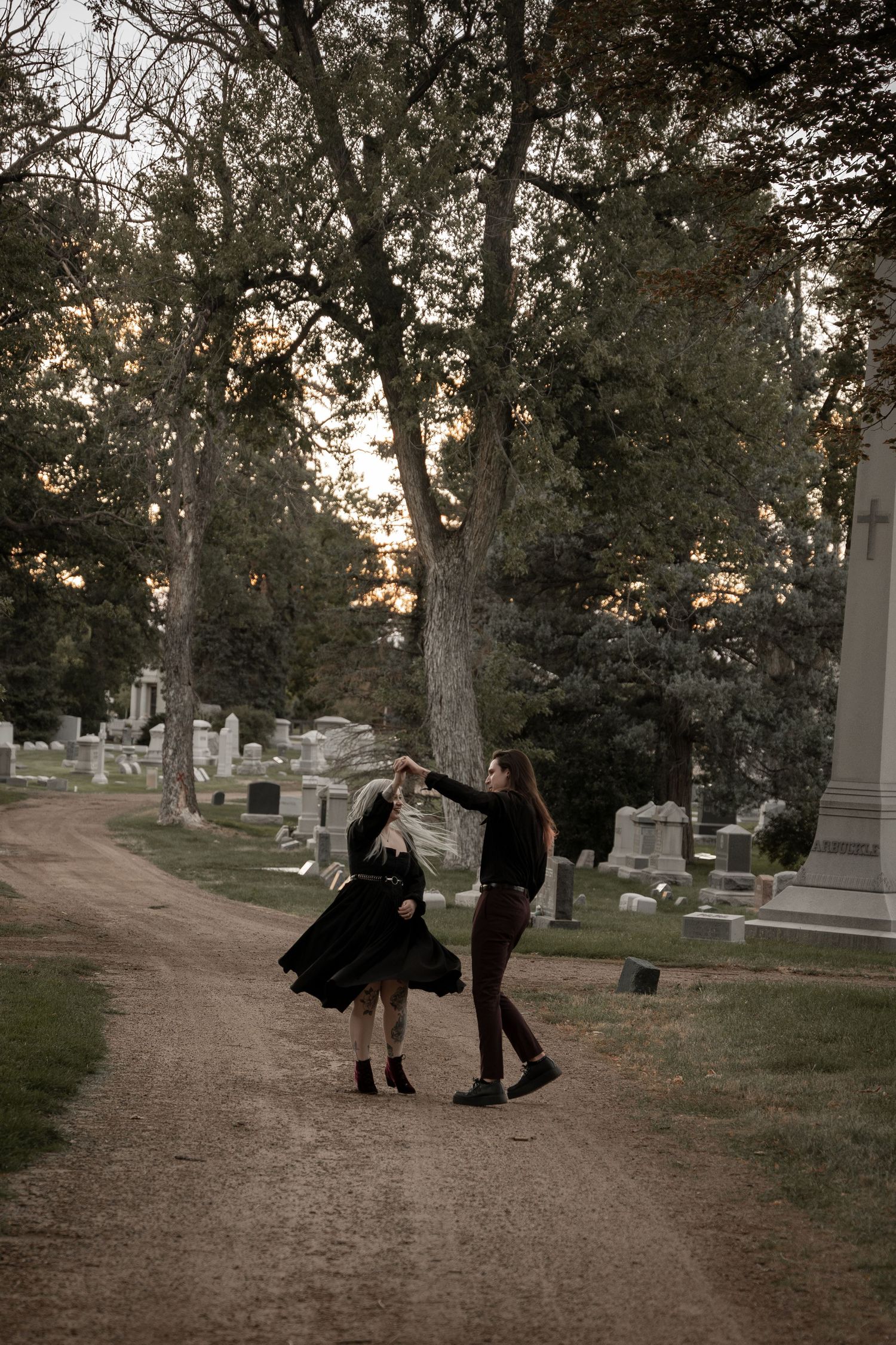 Sequence showing people in dark clothing dancing through a cemetery path at dusk.