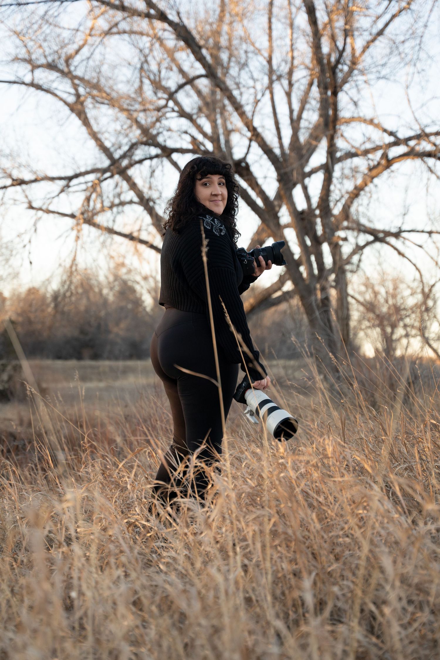 Person in black winter clothing walking through tall brown grass in a natural outdoor setting during autumn.