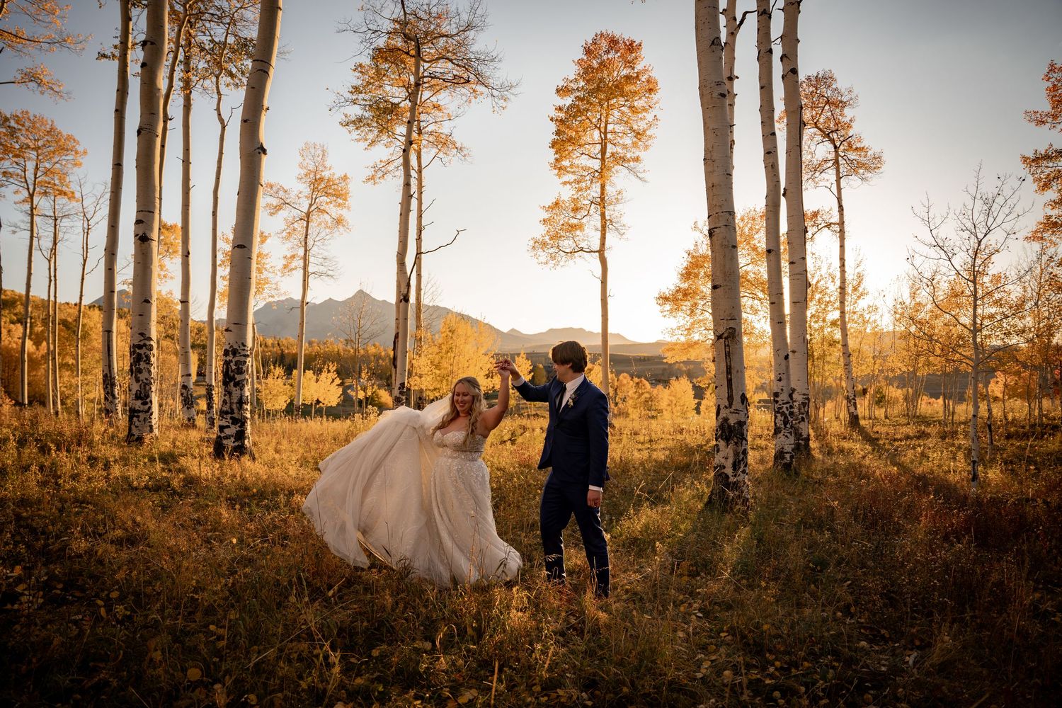 A couple dances through golden aspen trees at sunset in the mountains during their wedding celebration.