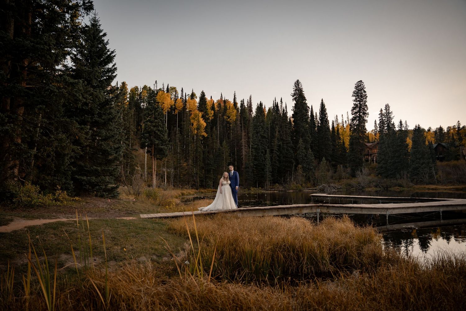 Scenic mountain wedding landscape with evergreen forest and lake reflection at dusk.