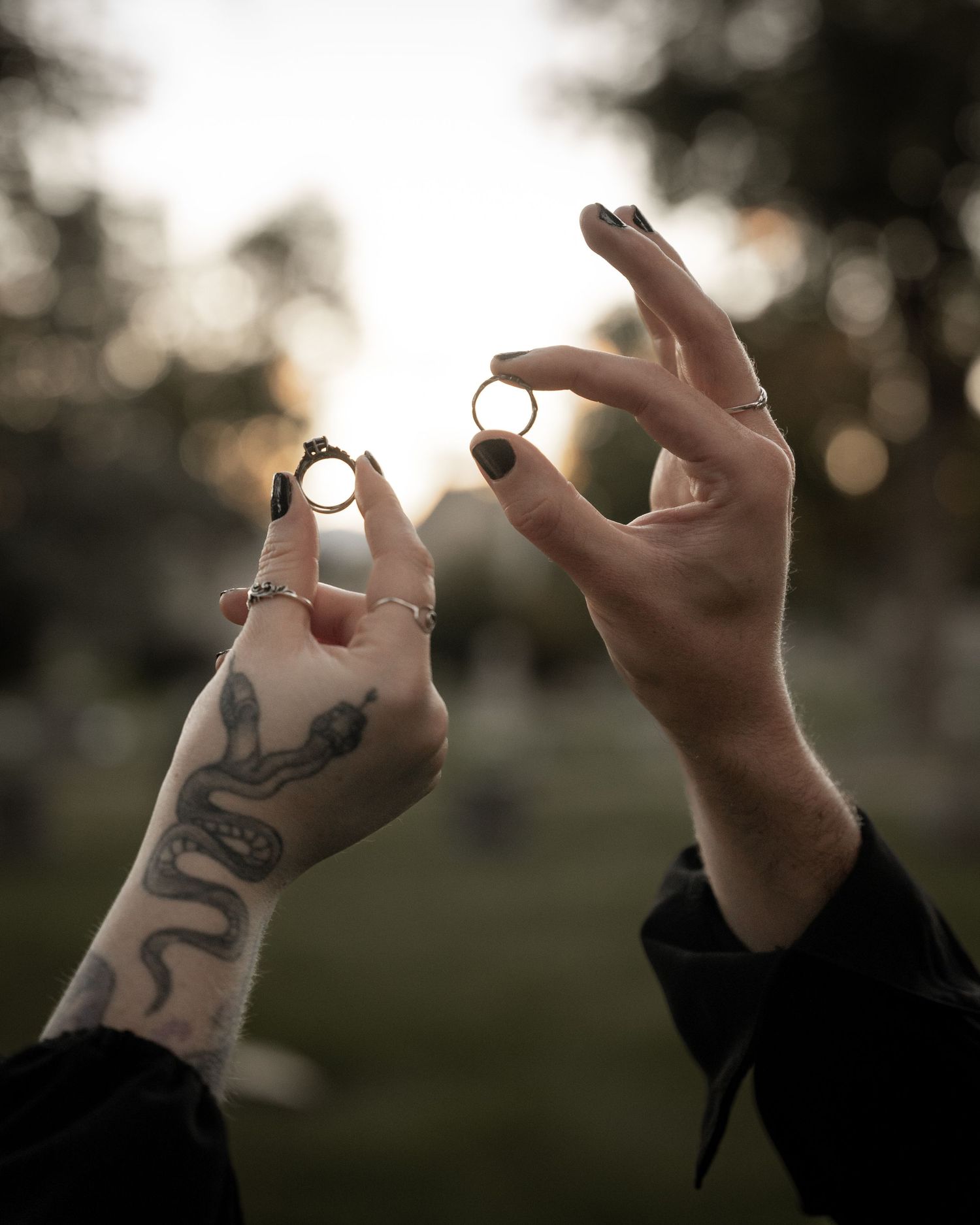 Close-up series of tattooed hands holding up rings against a blurred cemetery background.