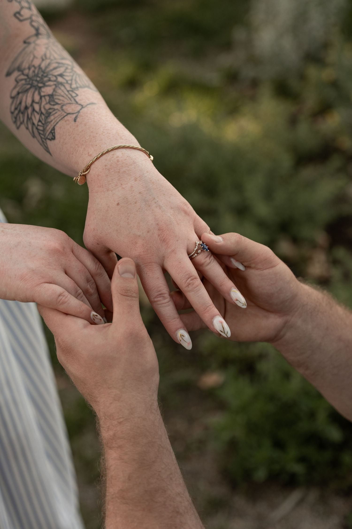 Close-up of hands exchanging a ring during a wedding ceremony, with a gold bracelet and floral tattoo visible.
