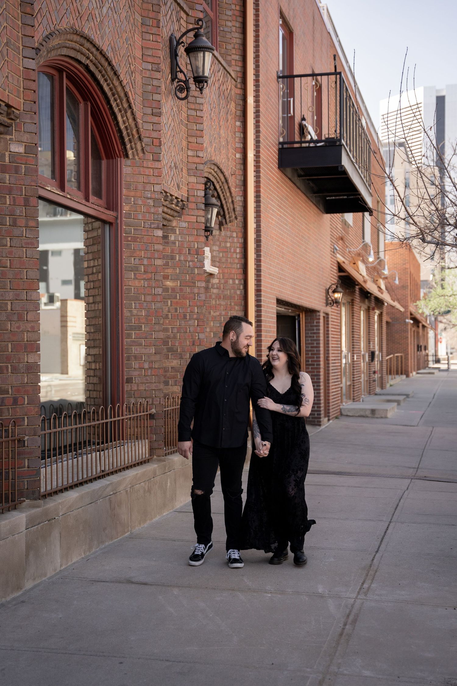 A couple walking together along a brick building sidewalk in urban setting.