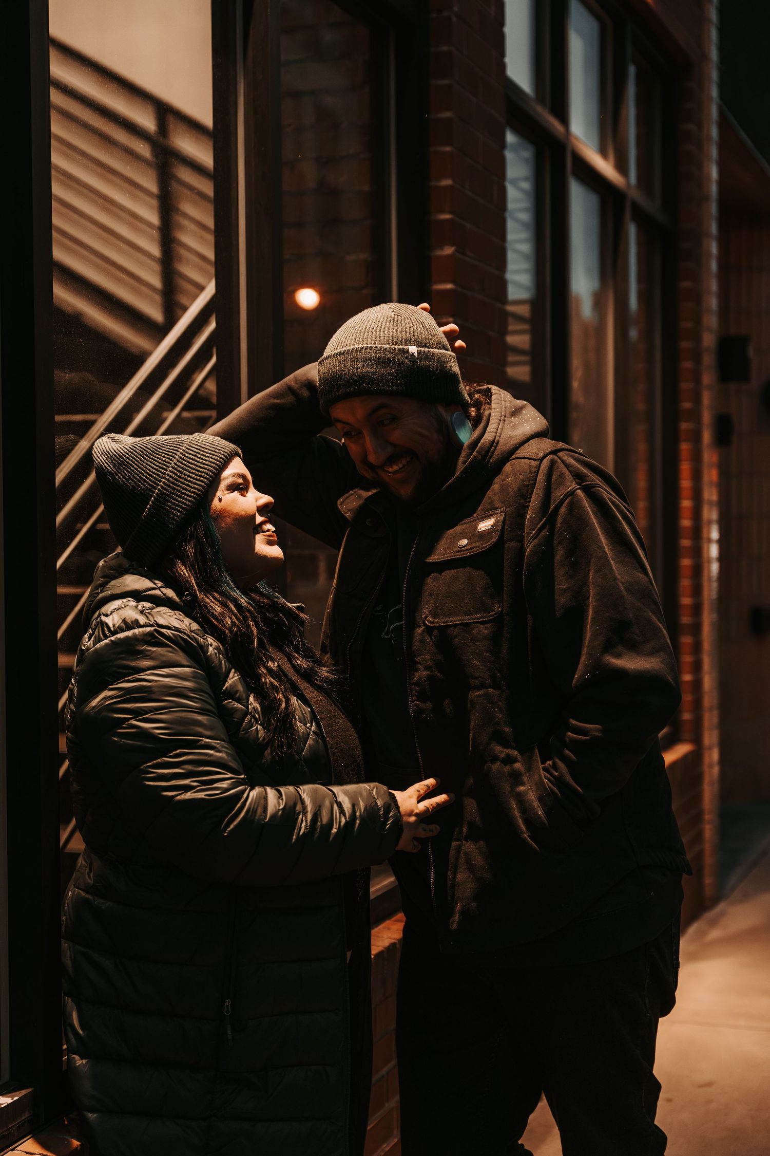 A couple sharing an intimate embrace in dark winter coats against an urban backdrop.