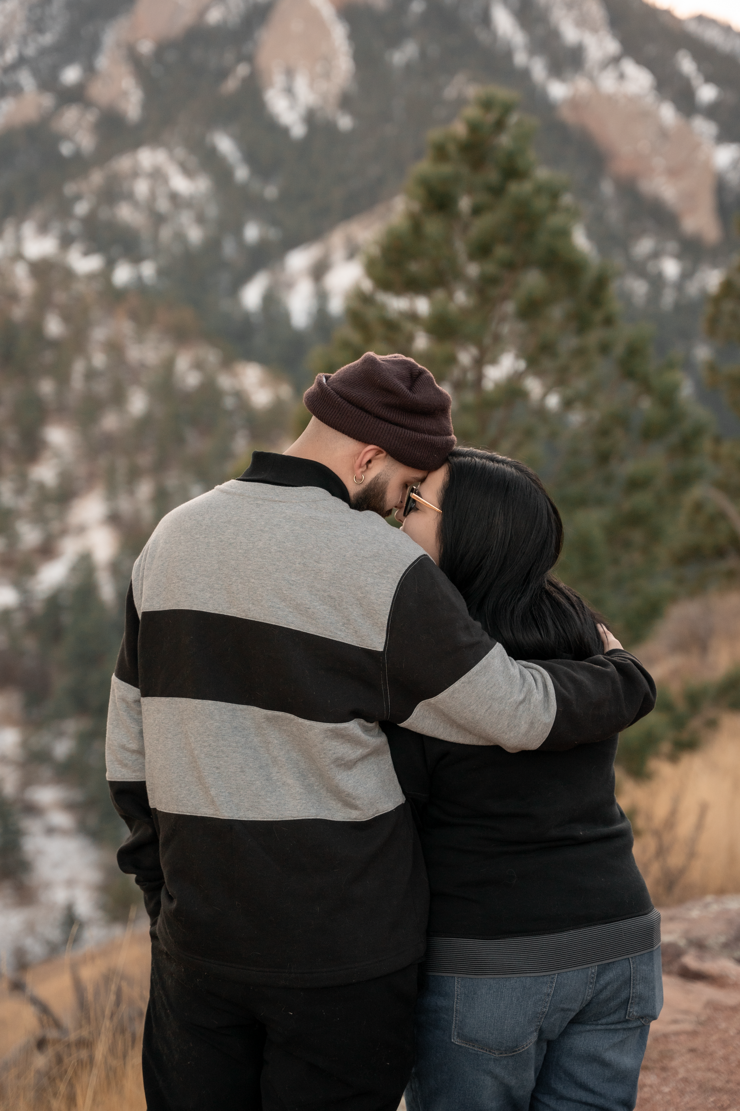 Couple embracing with foreheads touching against a scenic mountain backdrop in winter.