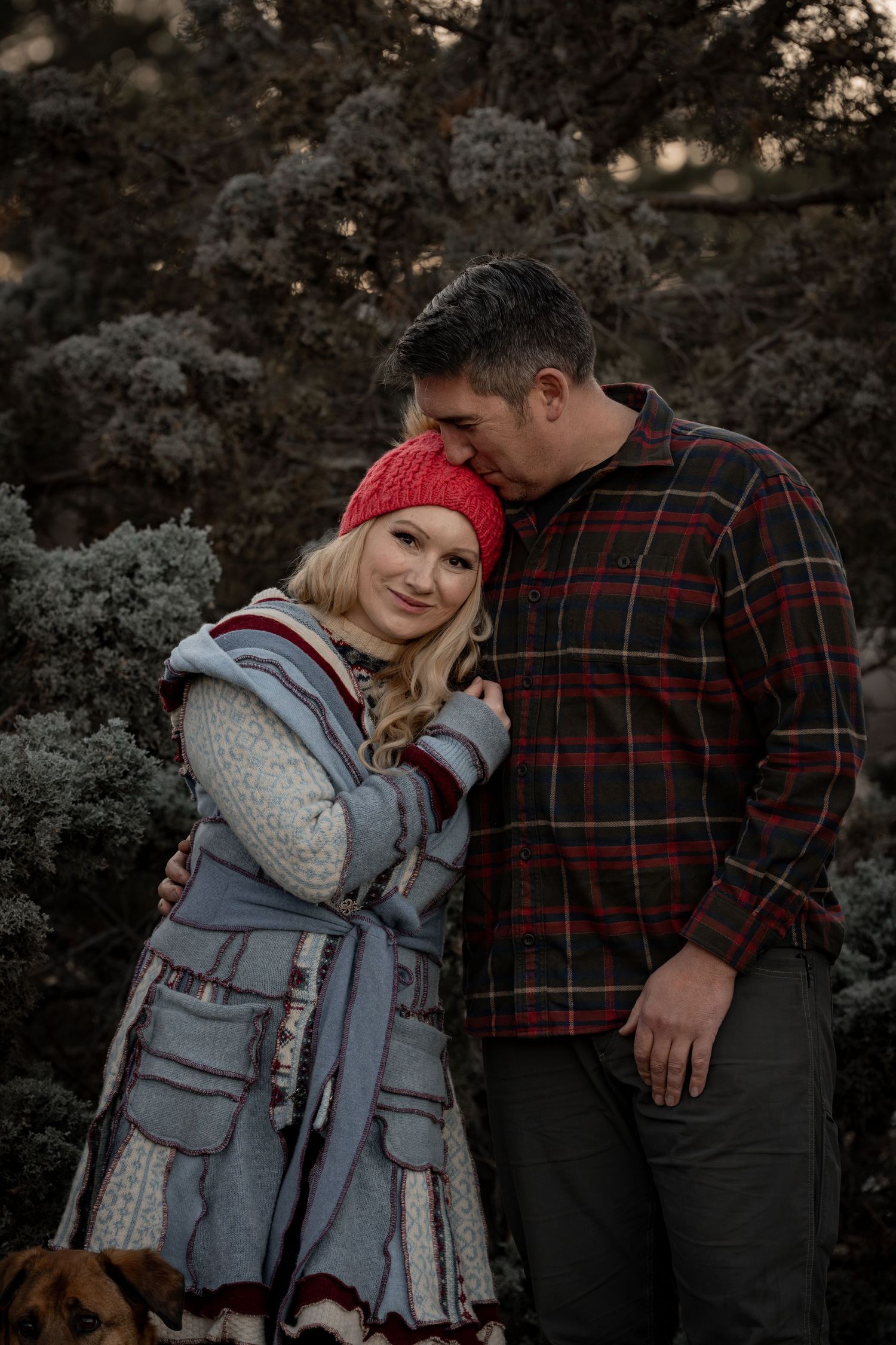 A couple poses together in winter clothing with plaid and knit details against a rocky backdrop.