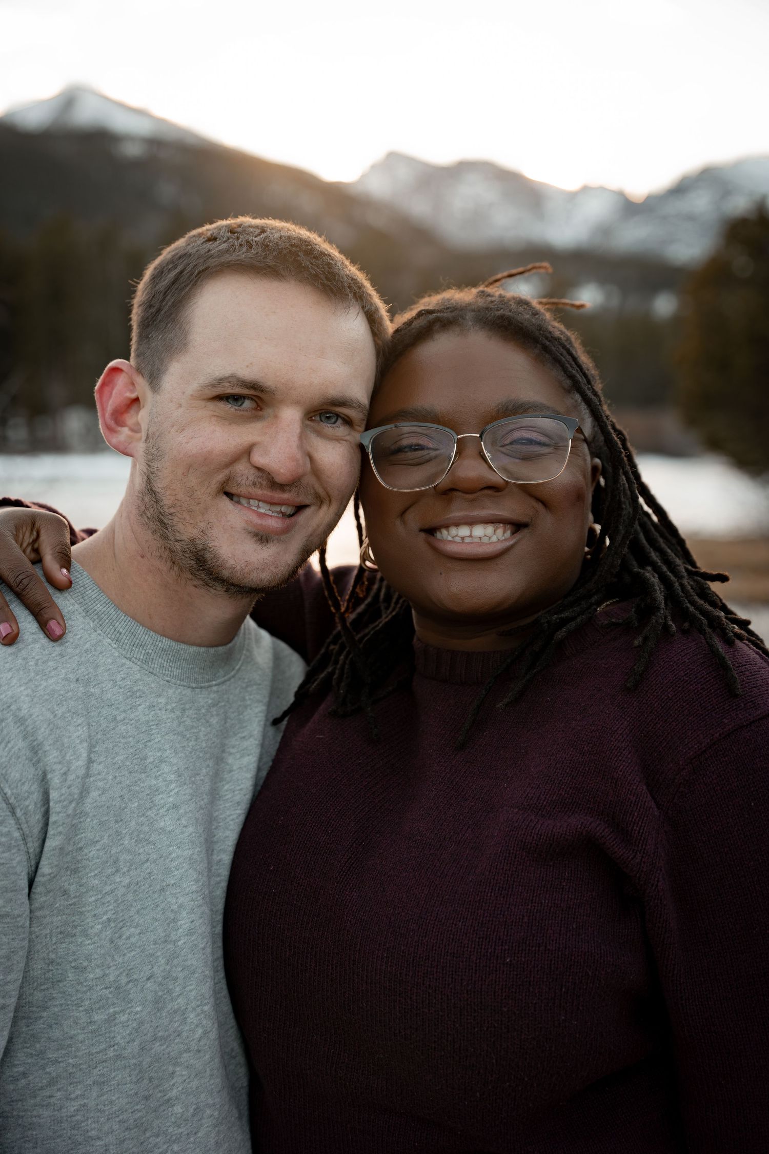 Smiling interracial couple posing together with snowy mountains and frozen lake in background.