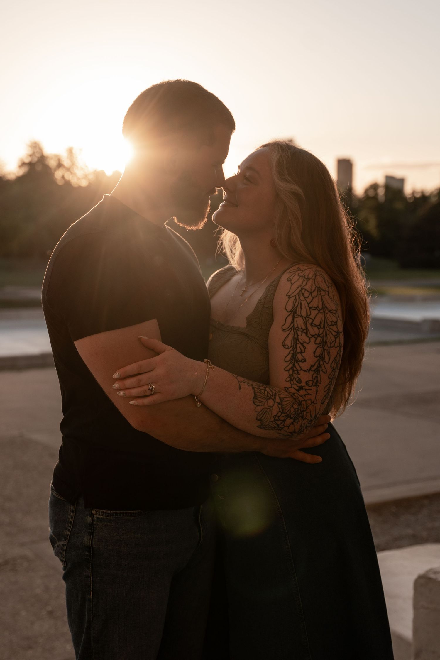 Couple sharing a romantic moment at golden hour sunset, woman with floral arm tattoo embracing man in warm backlit glow.
