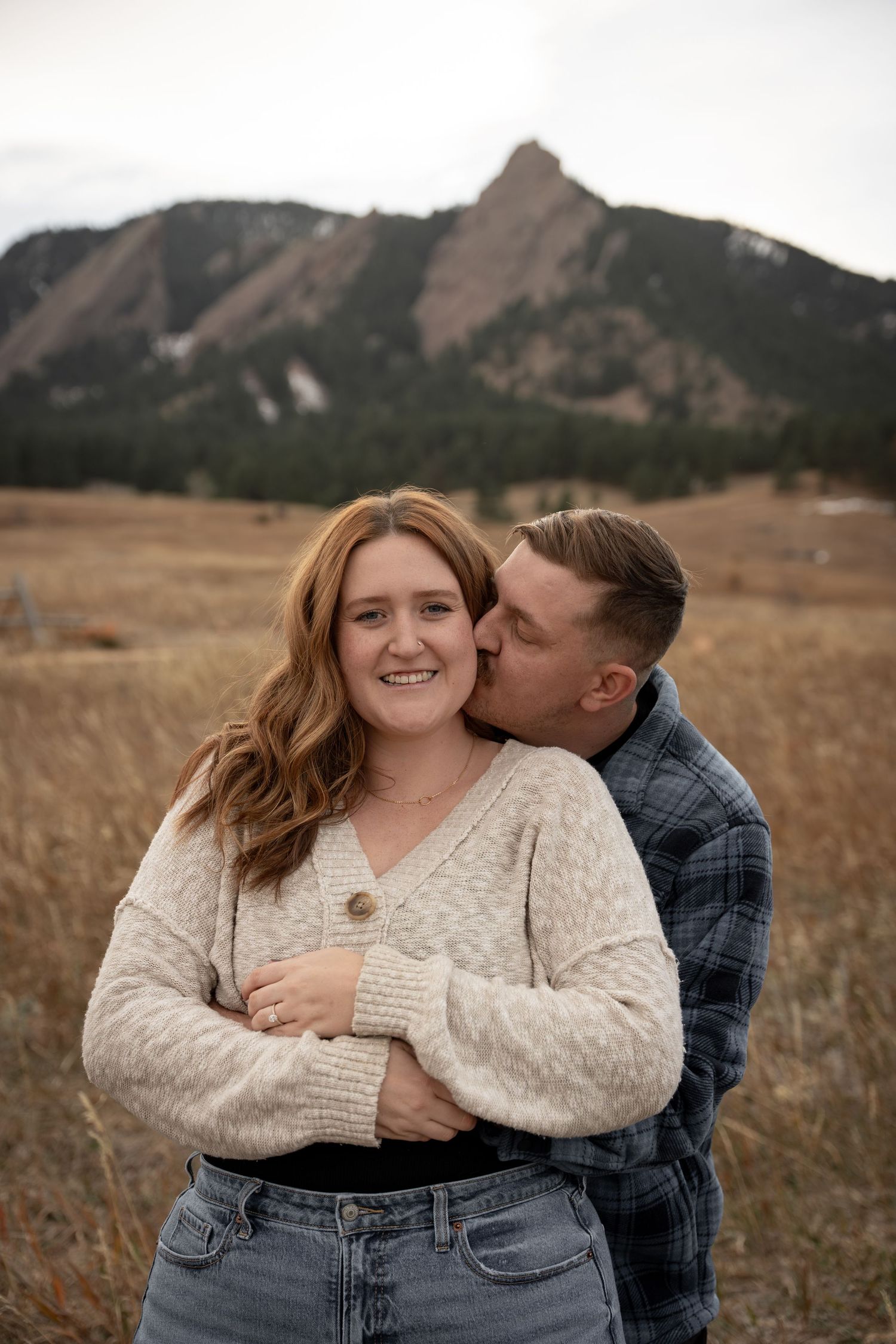 Couple embracing in a golden field with the Flatirons mountains of Boulder, Colorado in the background.