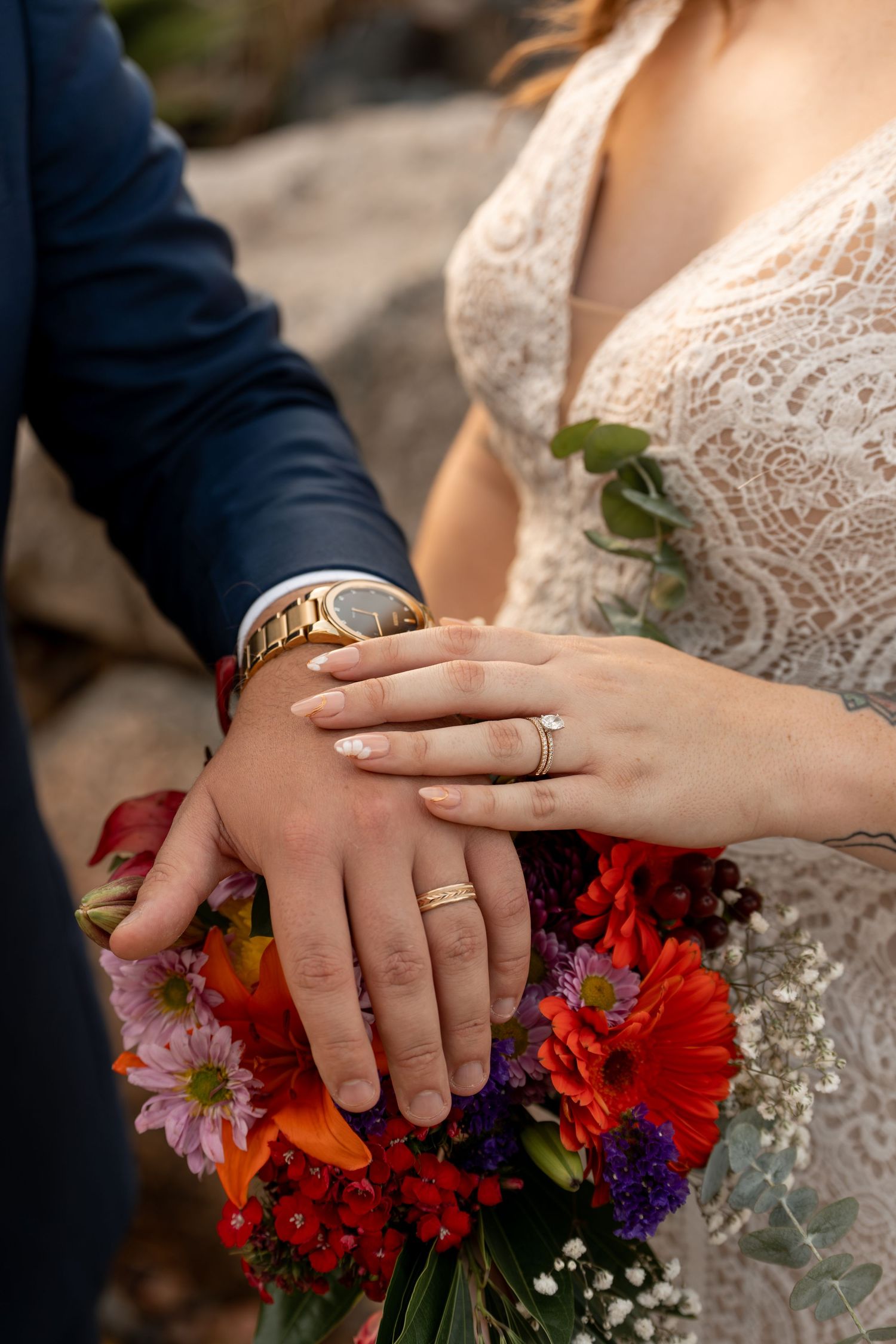 Close-up of wedding rings and hands on colorful bouquet.