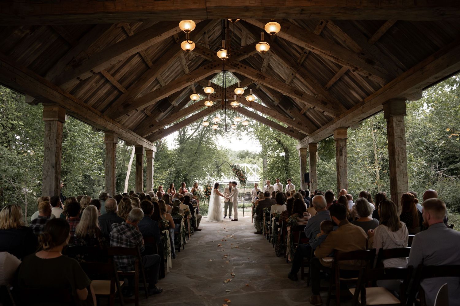 Rustic wooden reception venue with hanging lights and guests seated at long tables.