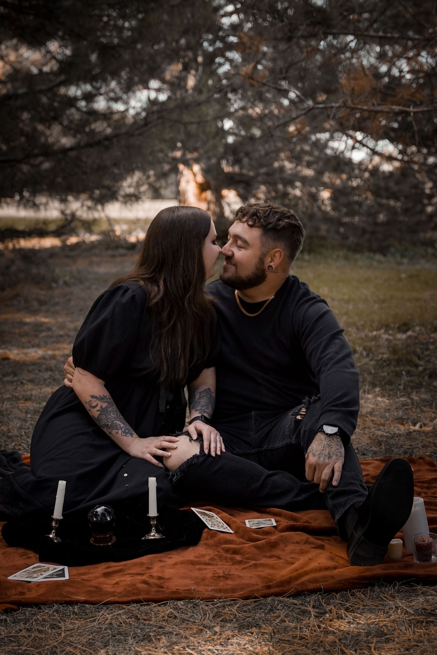 A couple shares intimate moments while relaxing on a brown blanket in a moody outdoor setting at dusk.