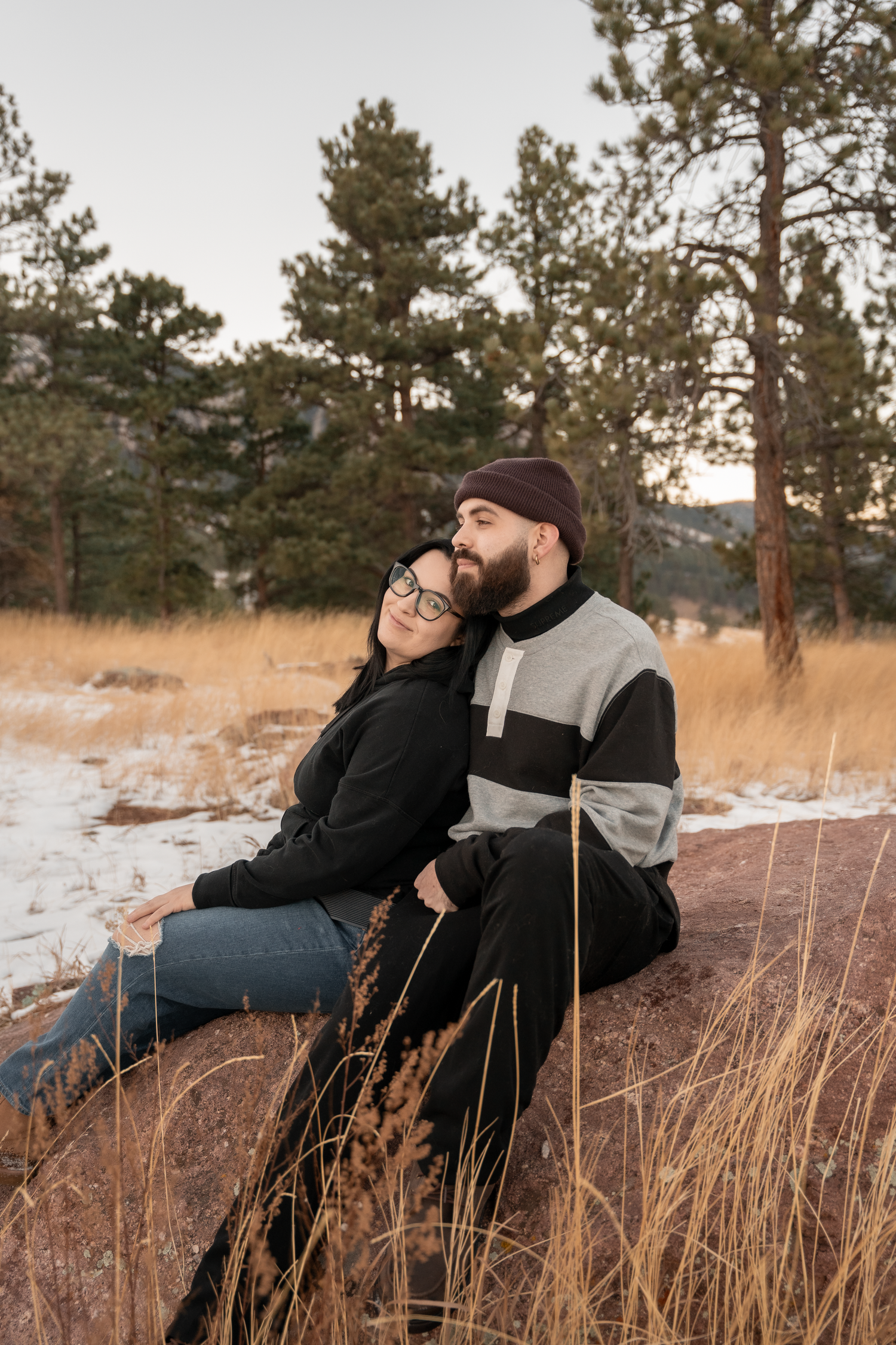 A couple relaxes together in tall grass during a winter mountain photoshoot.