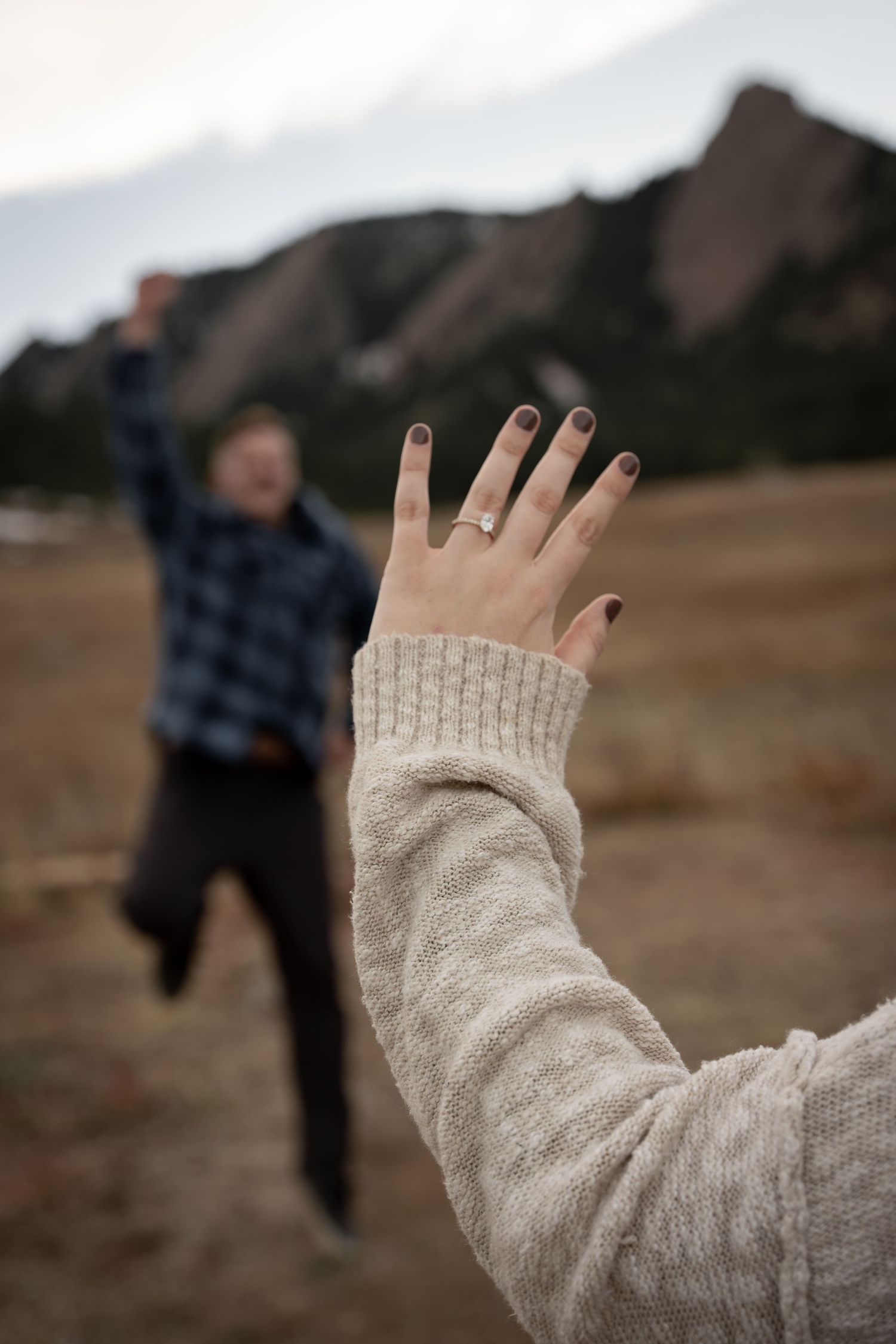 A hand in a beige sweater waves goodbye with a blurred figure walking away in the background.