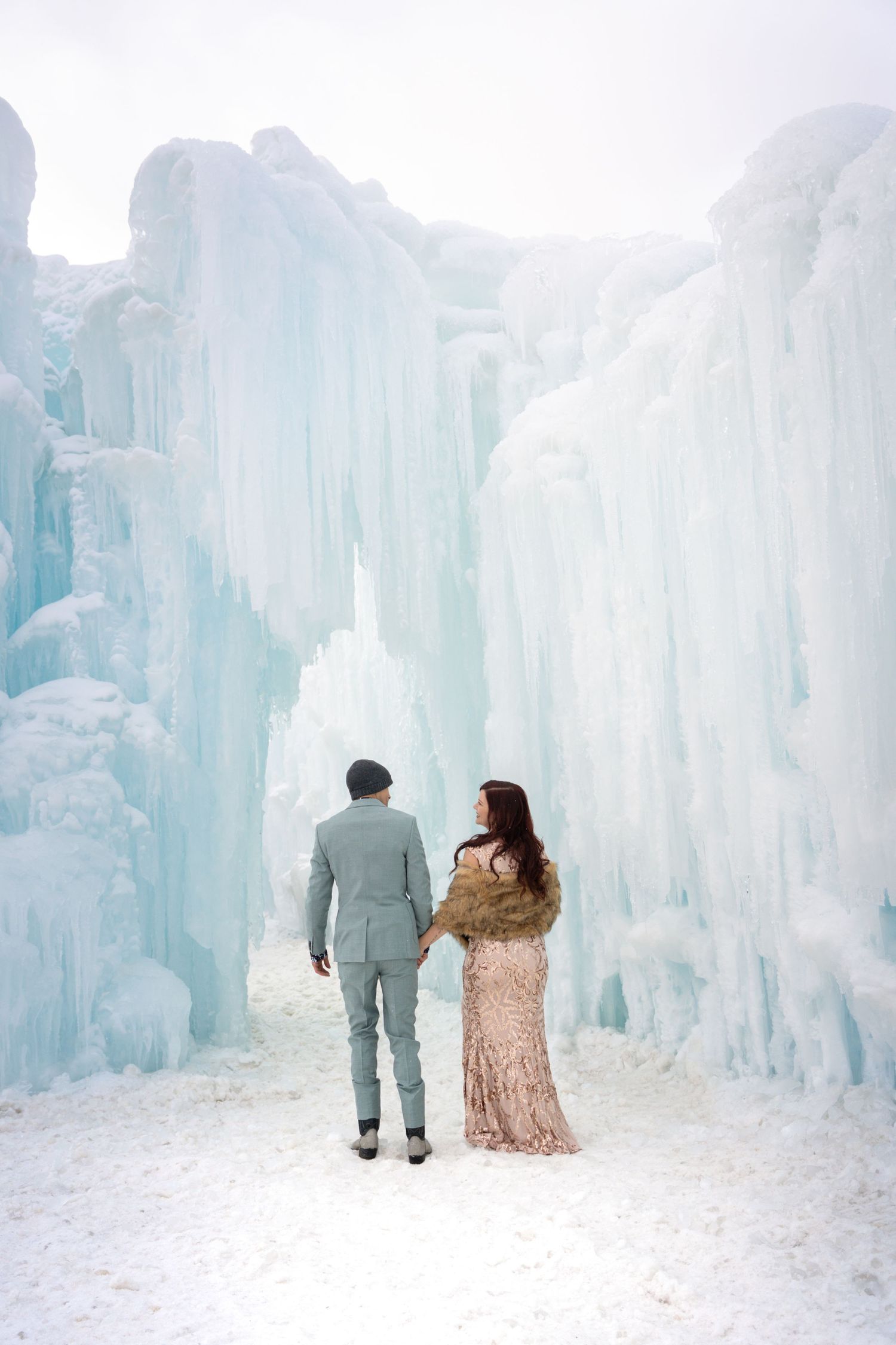 Couple walking through magical ice castle corridors illuminated with soft blue lighting.