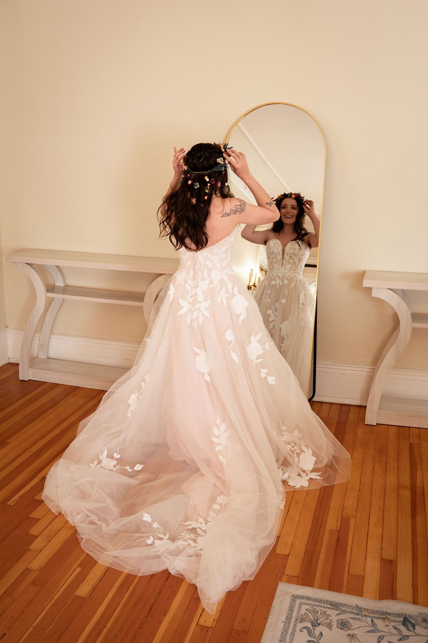 Bride to be wearing a beautiful floral gown adjusts her flower crown in the mirror while getting ready.