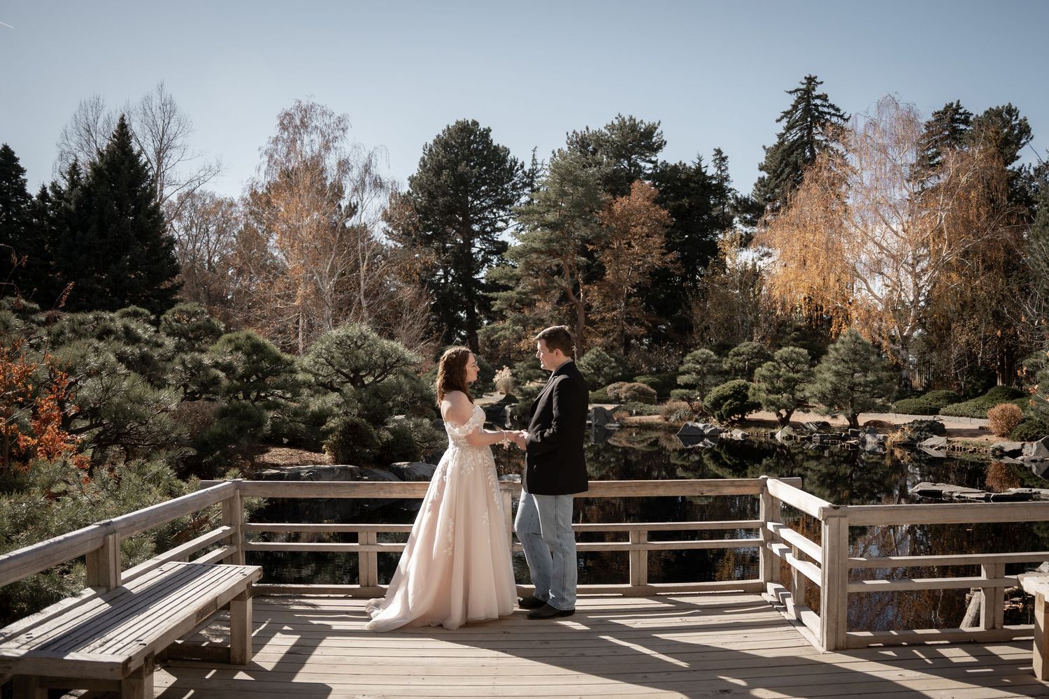 A person in a wedding dress poses on a wooden deck with mountain scenery in the background.