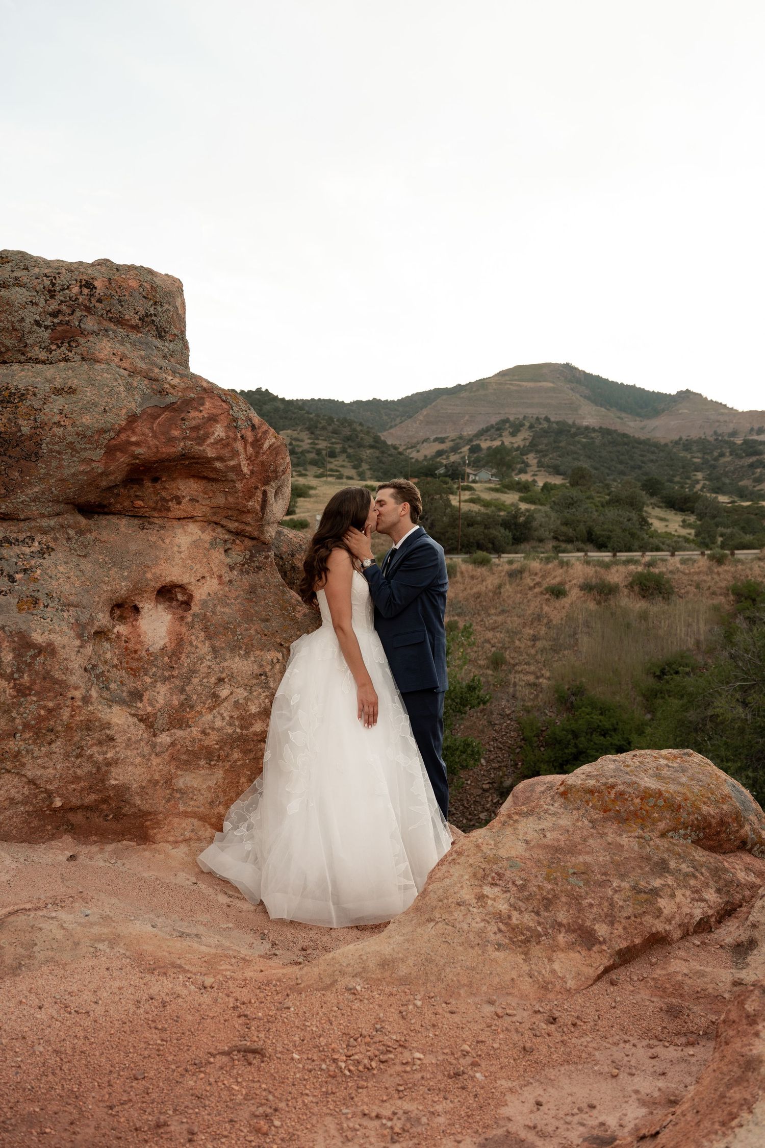 Wedding couple embraces on red rock formations in desert landscape.