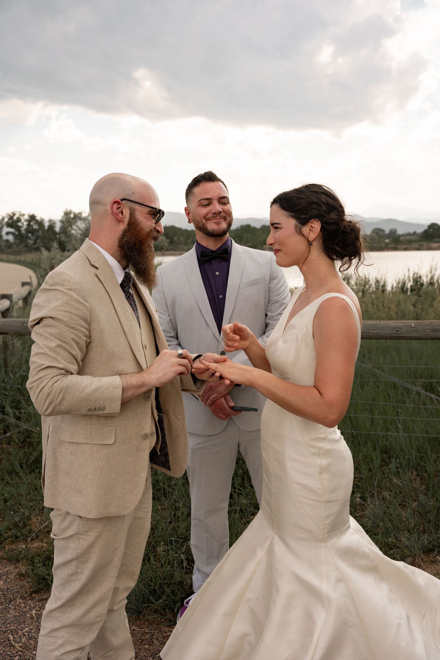 Wedding celebration moment with guests in beige and gray suits by a lake.