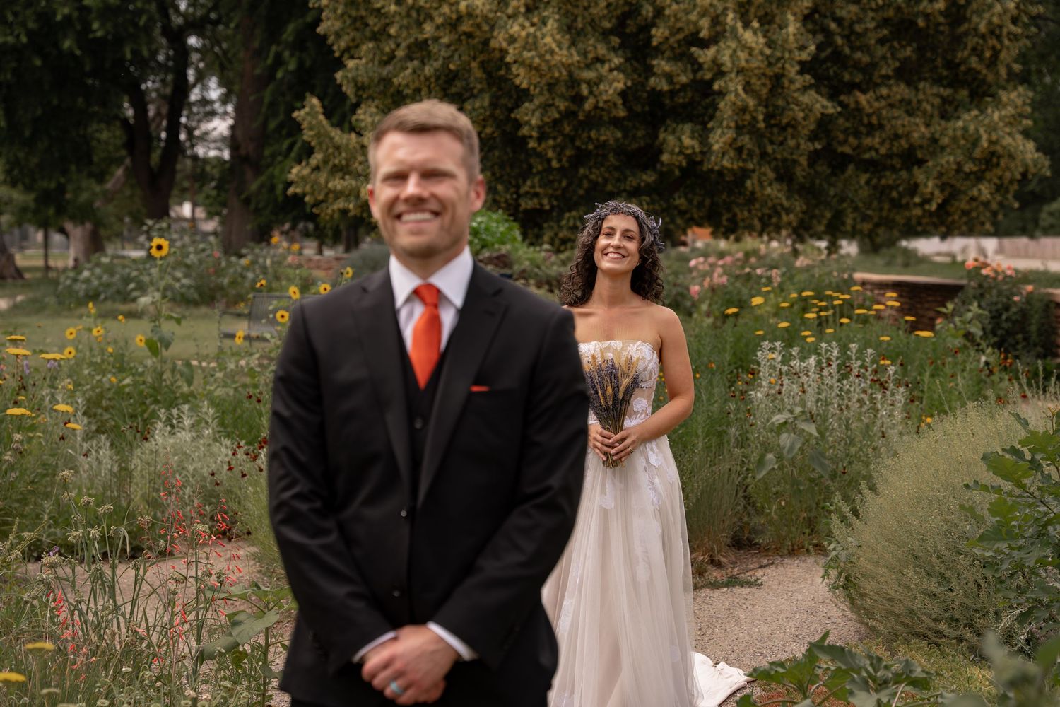 A first look wedding moment captured in a garden setting with a bride standing behind a groom in formal attire.