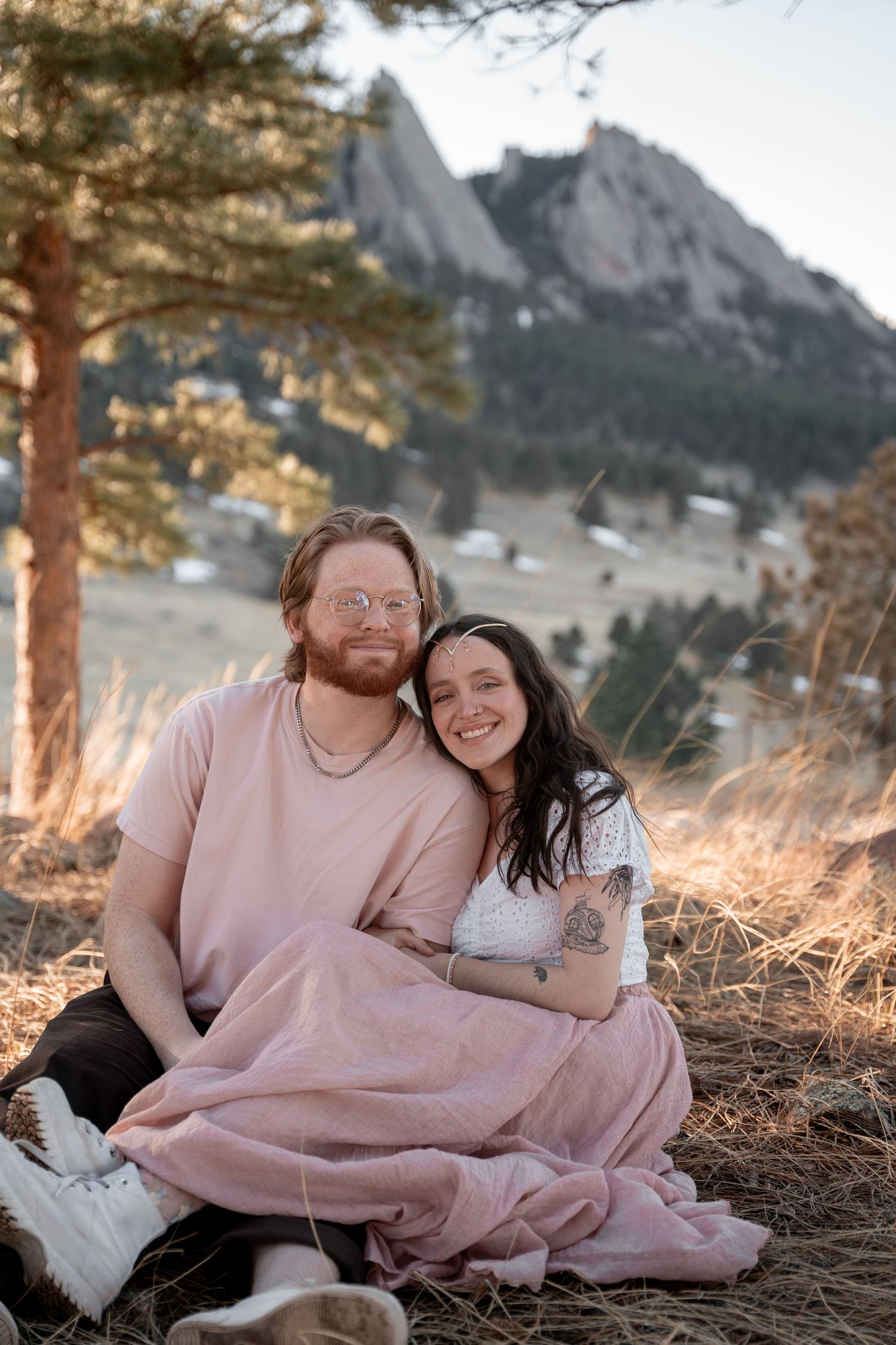 Couple sitting together on a hillside at Chautauqua Park in Boulder, Colorado, wrapped in a pink blanket with the Flatirons behind.