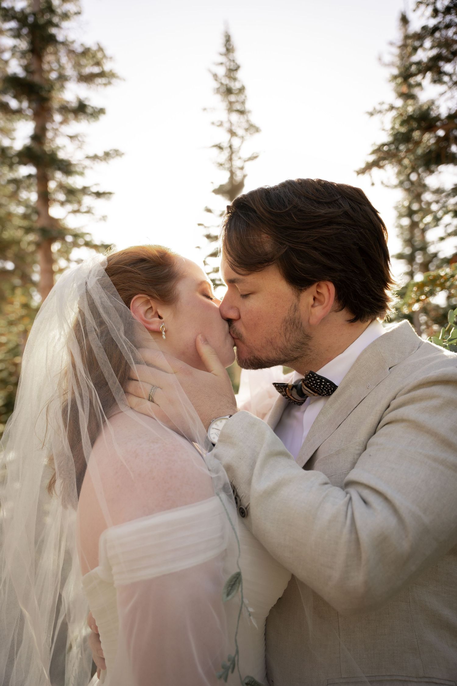 A sequence of romantic wedding photos showing a couple kissing in front of evergreen trees at sunset.
