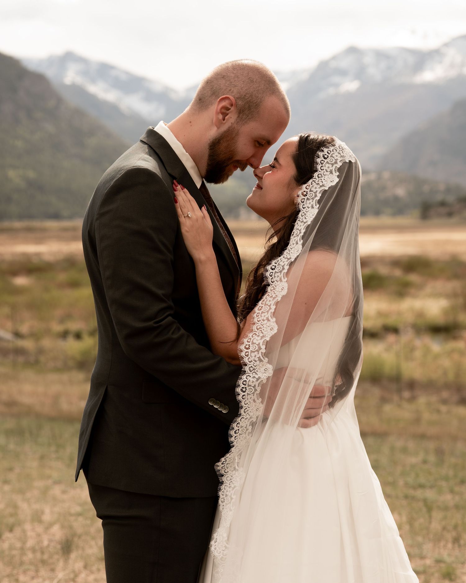 Couple shares an intimate moment in wedding attire with snow-capped mountains backdrop in Rocky Mountains.
