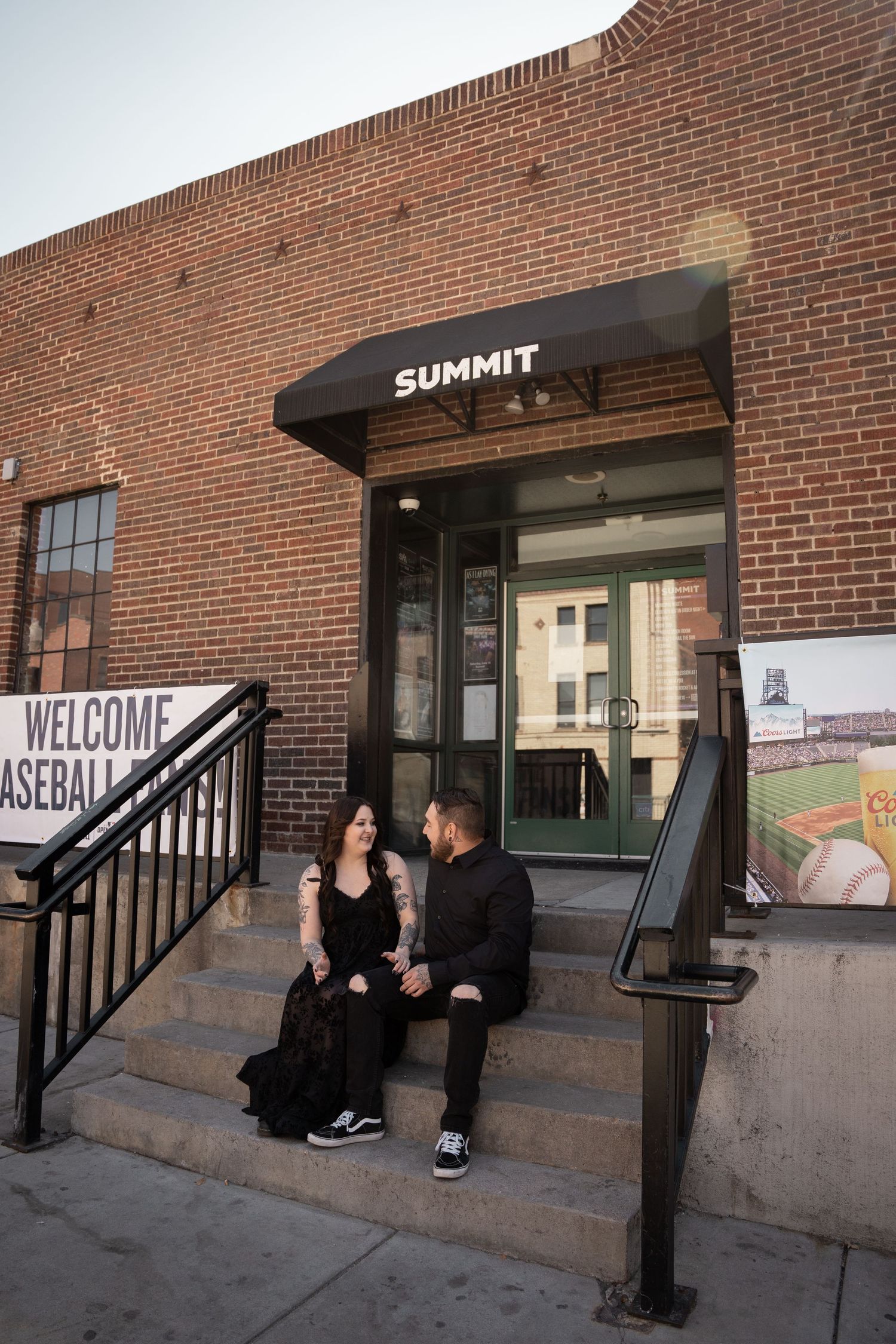 Couple sitting on steps outside Summit venue entrance, sharing a moment beneath the awning on a brick building.