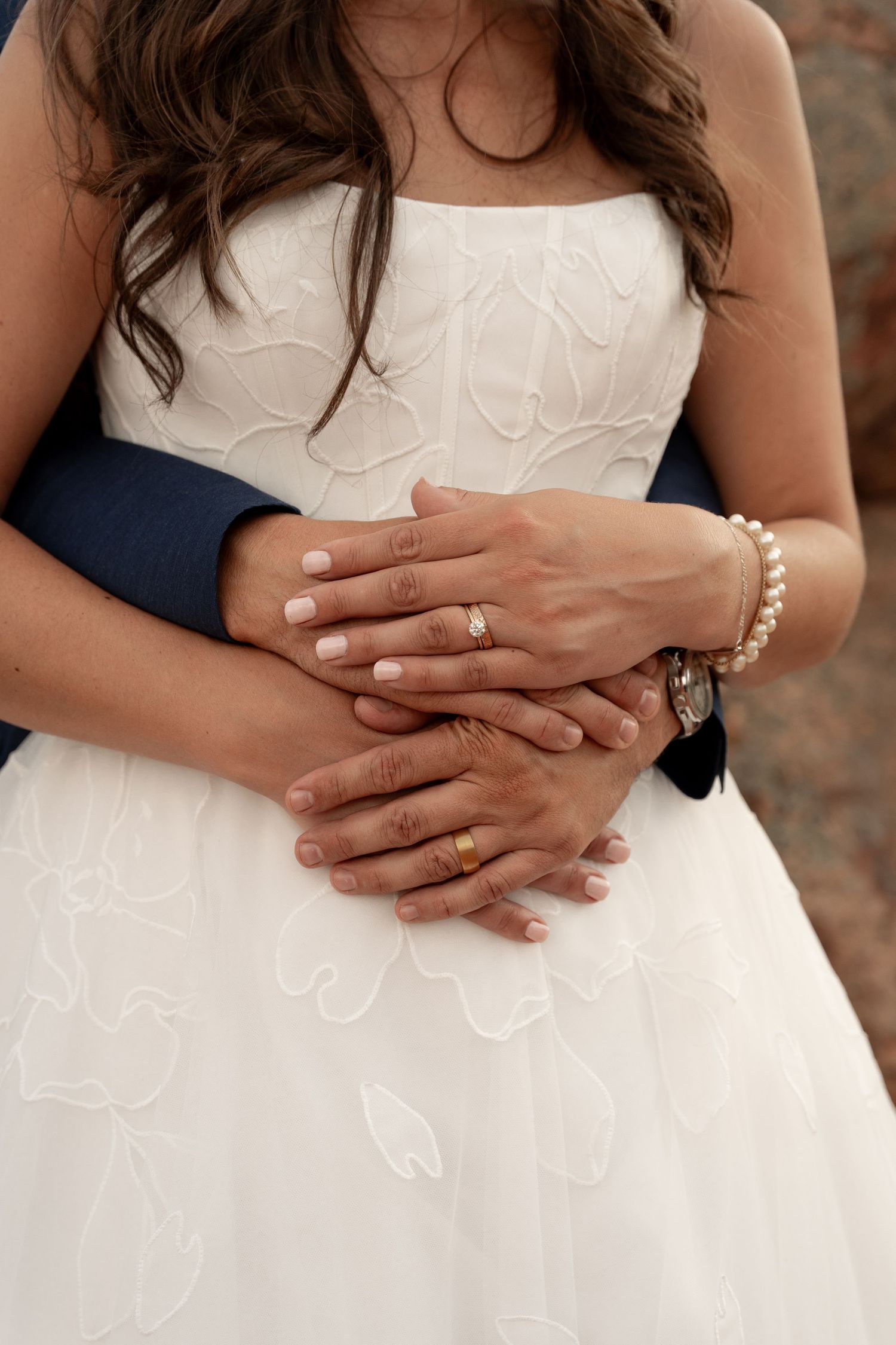 Close-up series of hands with wedding rings and pearl bracelet against white dress details.
