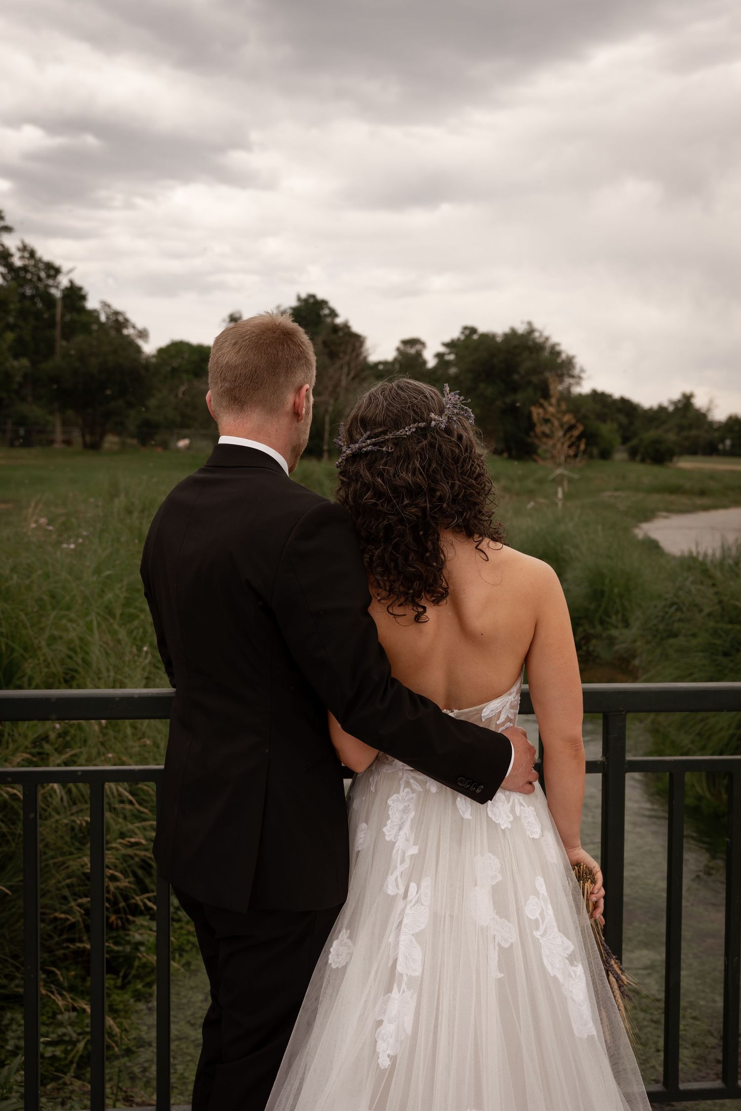 A couple in wedding attire share an intimate moment on a balcony overlooking a scenic natural landscape.