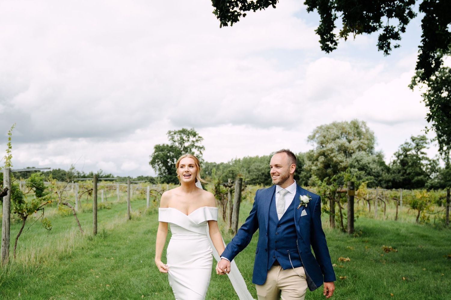 An intimate outdoor wedding photograph of a bride and groom laughing together among vineyard rows.