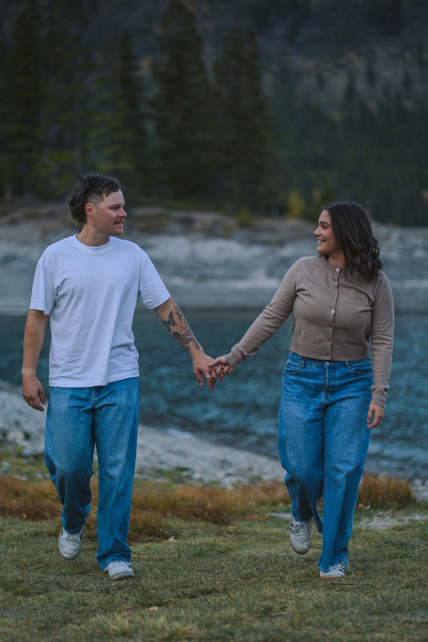 walking hand in hand at Lake Minnewanka for a sunset engagement shoot.