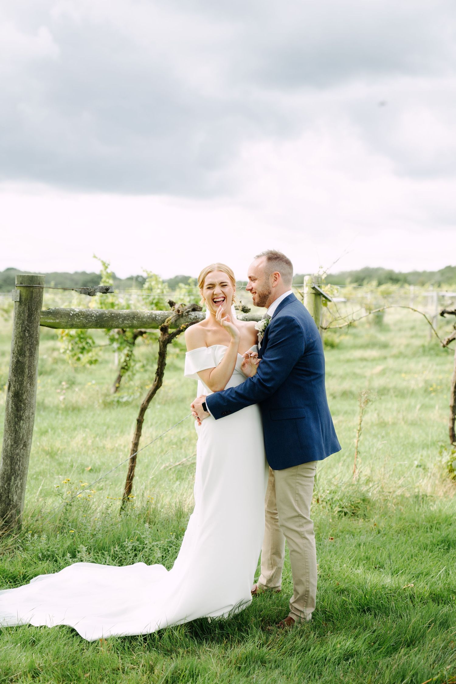 An intimate outdoor wedding photograph of a bride and groom laughing together among vineyard rows.